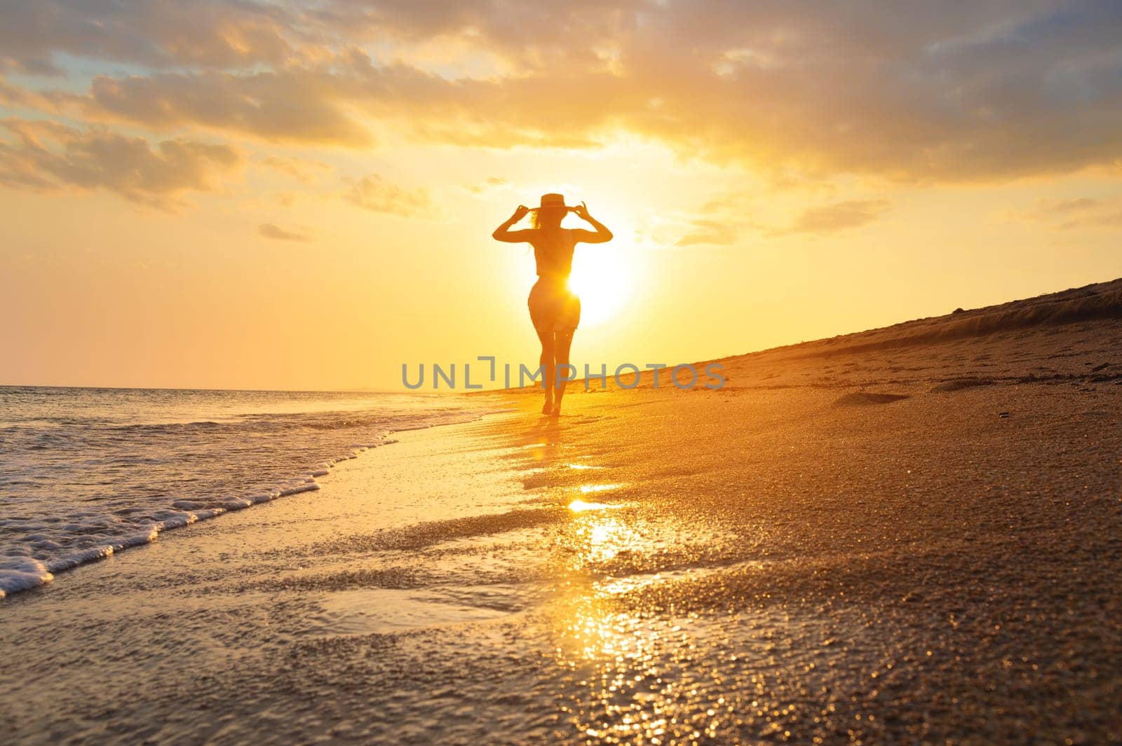 Seascape during golden sunrise with beautiful sky. Woman on the beach. Young happy woman walks along the seashore. A girl looks at a magical sunrise.