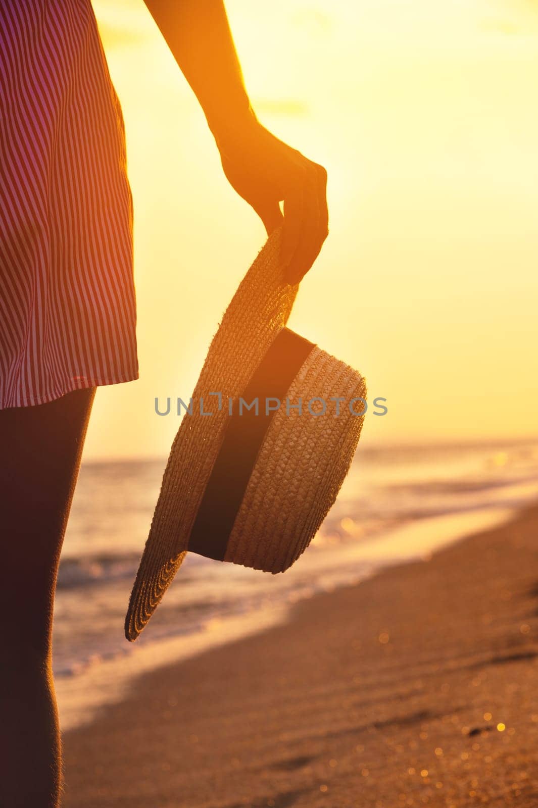 Young woman on the beach holding a straw hat near her feet close-up, sea coast.