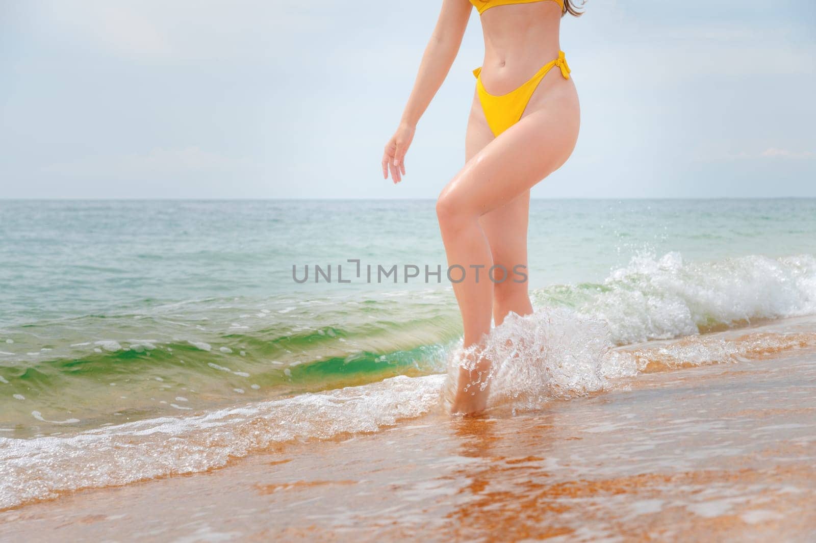 young woman walking along the beach, close-up. a girl cheerfully walks into the sea with waves with a golden sandy beach along the coast.