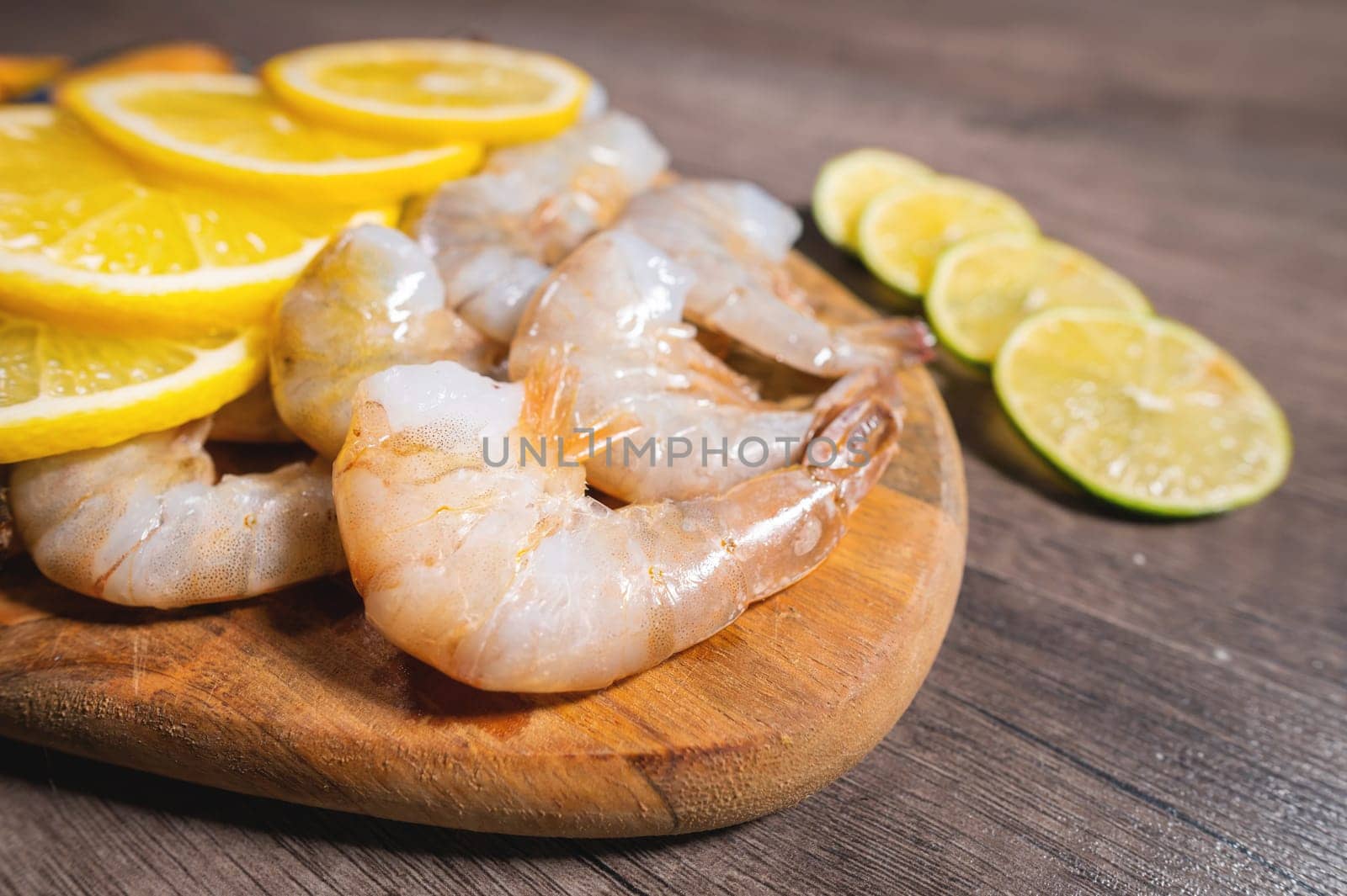 Boiled shrimp in the shell without a head and lemon wedges on a serving wooden plate, close-up of an appetizer.