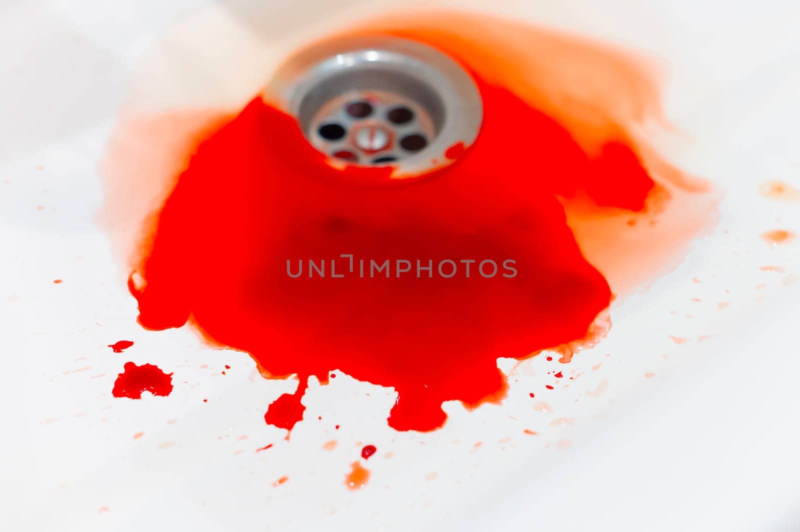 Blood flows over a white bathroom sink. Blood stains in the drain hole. Sink with streams of blood. Red paint drips down the sink drain. Accident with human injuries. Bleeding in the bathroom.