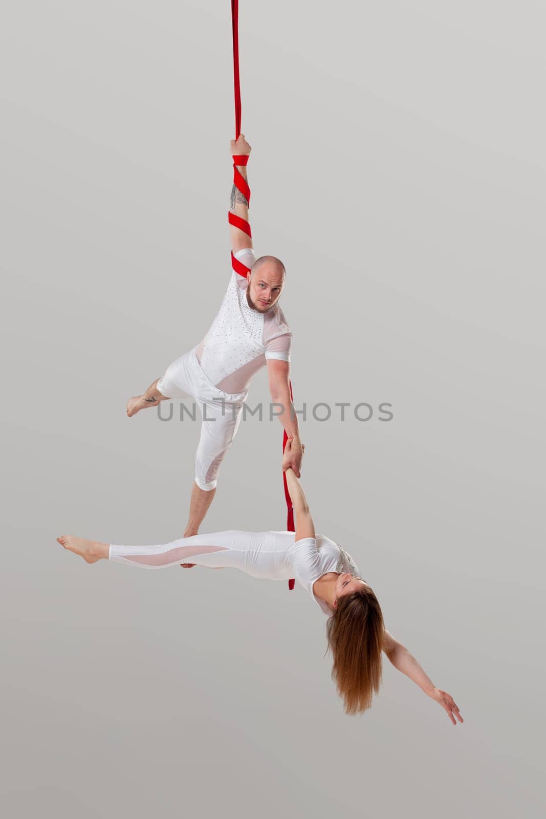 Beautiful girl and an athletic man in a white sport suits are performing an acrobatic elements in a studio. by nazarovsergey