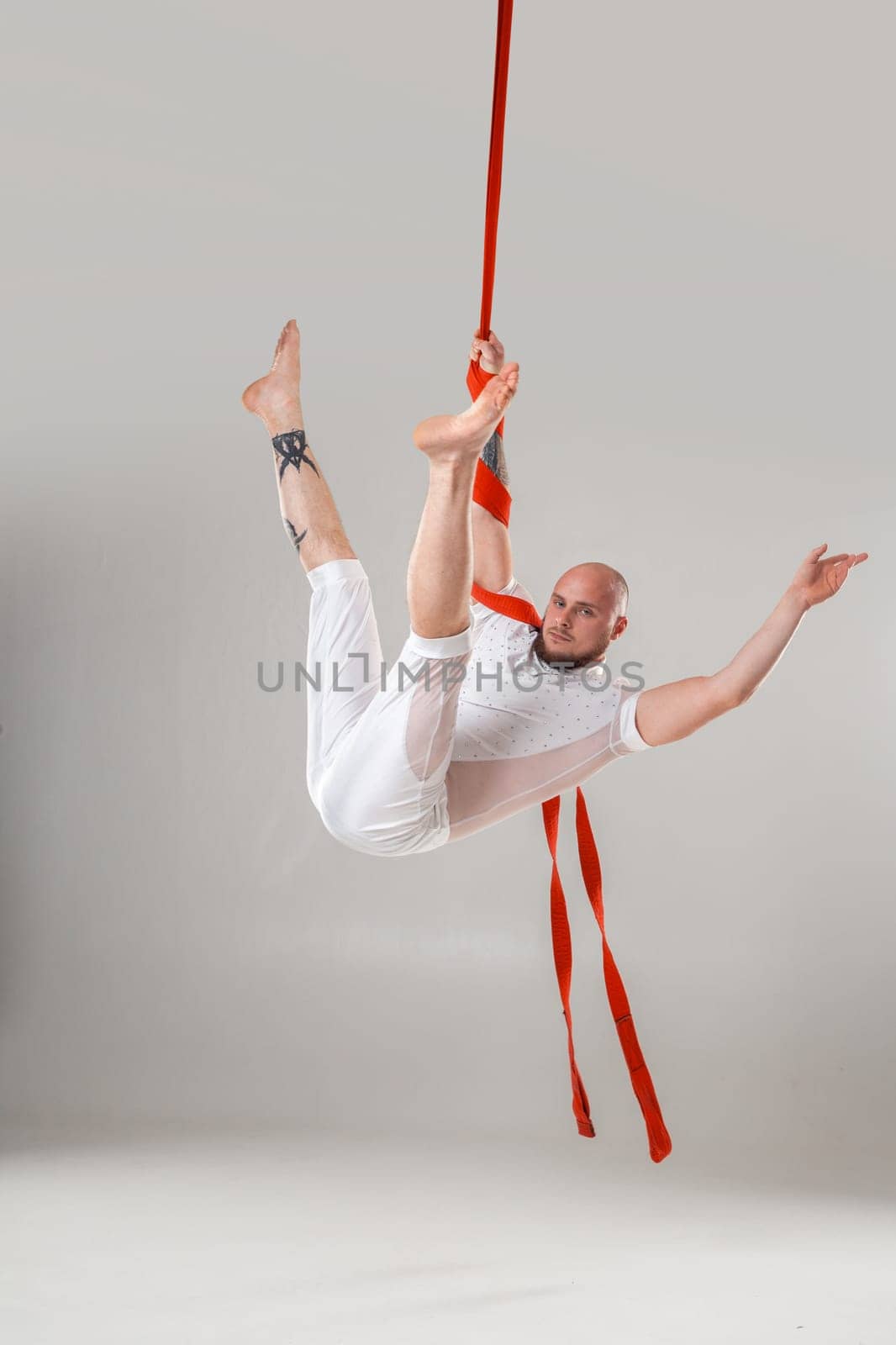 Gymnast performance on a red canvases. Athletic male in a light sport suit is doing an acrobatic elements in a studio isolated on white background. Dancing in the air with balance.