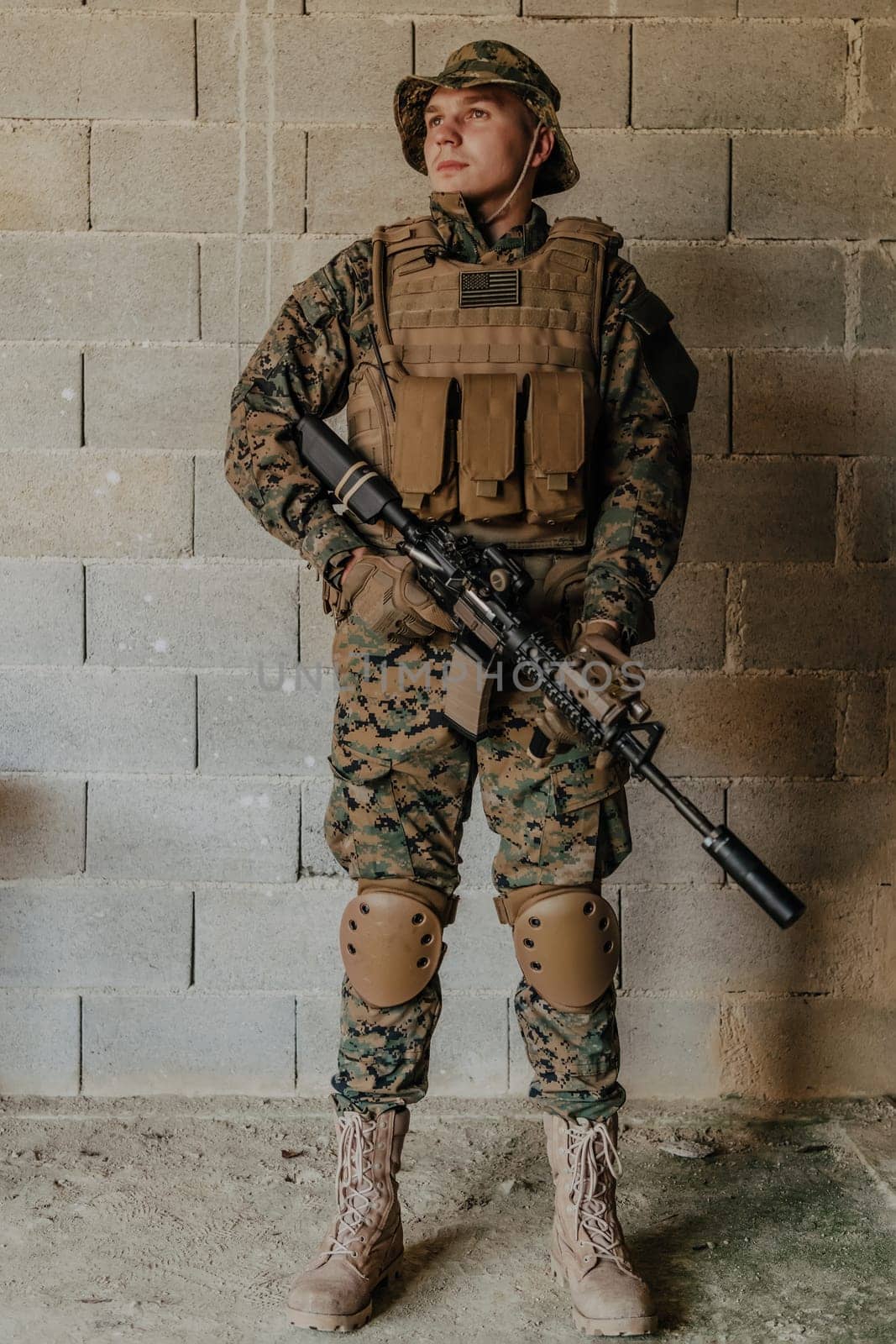 A soldier in uniform stands in front of a stone wall in full war gear preparing for battle.