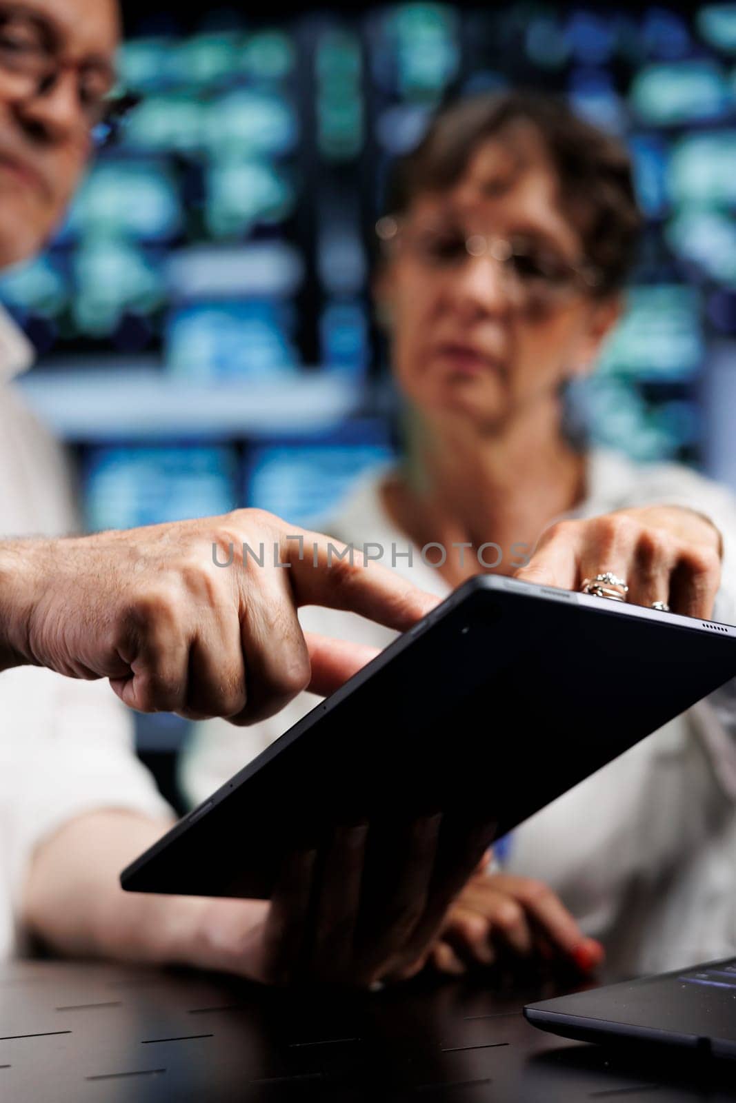 Elderly engineers working to maintain uptime in high tech data center. Experienced technicians brainstorming solutions to server hub infrastructure crashing, trying to repair equipment, close up