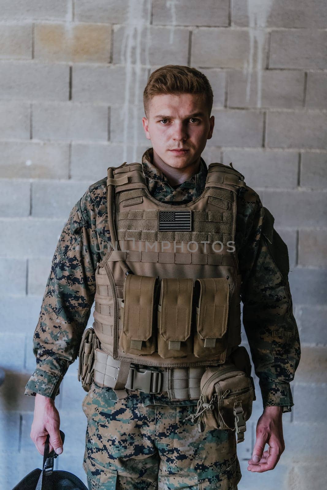 A soldier in uniform stands in front of a stone wall in full war gear preparing for battle.