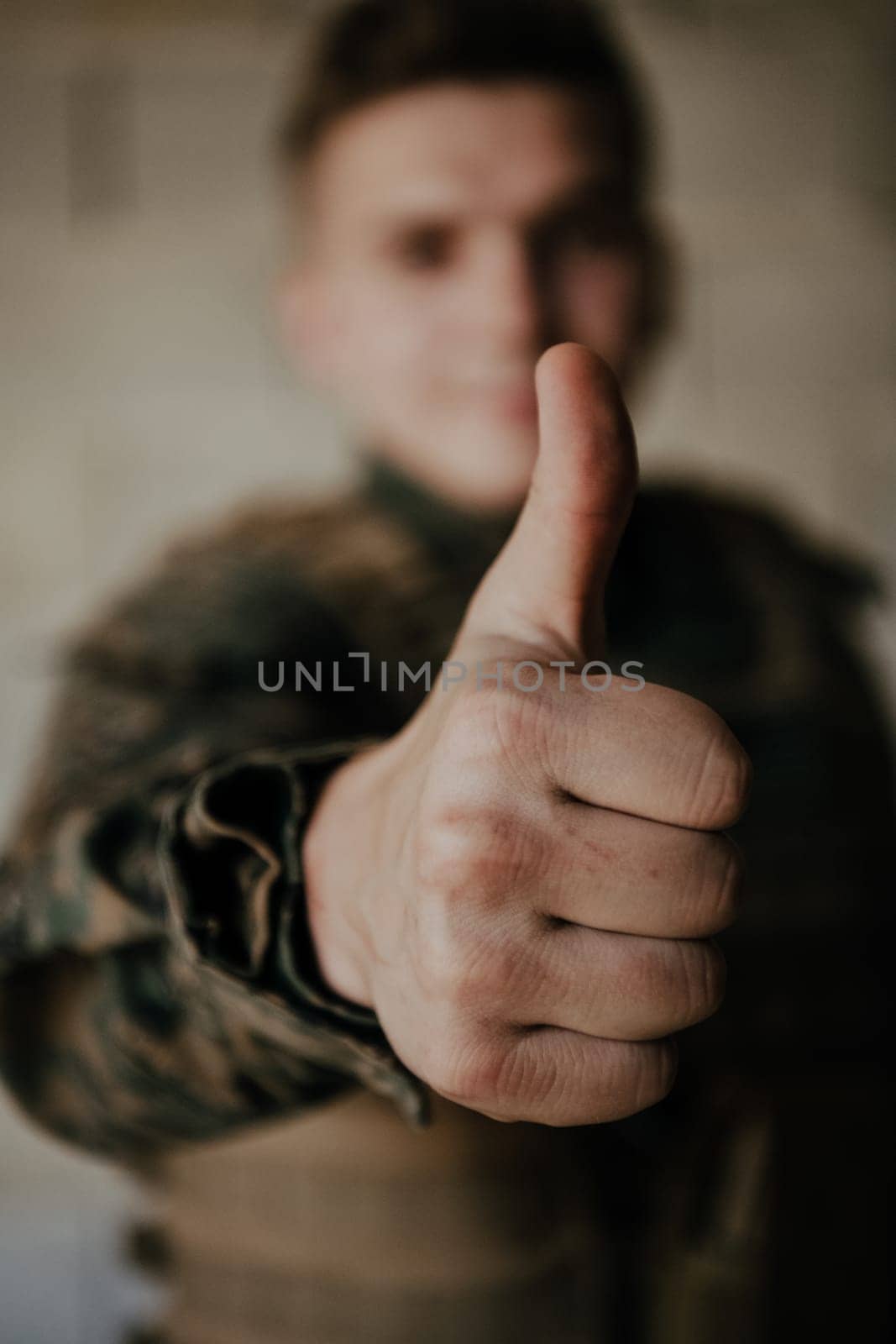 The soldier makes a gesture of success with his hand. A soldier in full war gear stands in front of a stone wall and shows the ok sign with his finger.