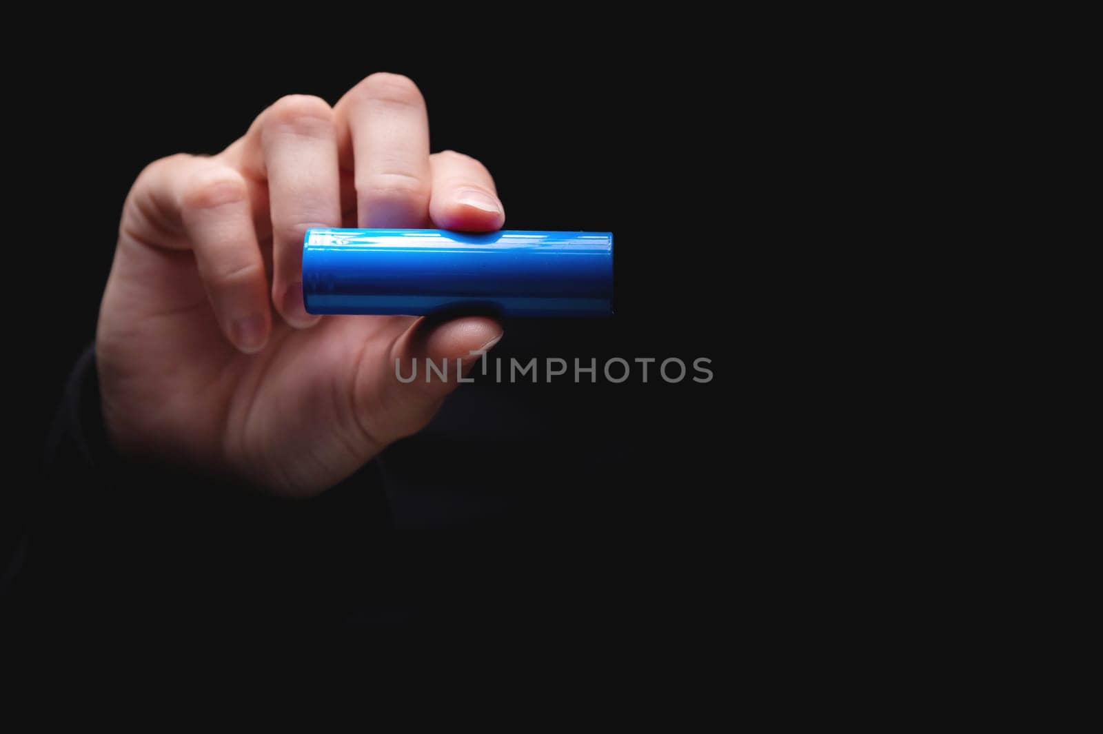 Lithium-ion battery for power in a human hand, on a black background. Woman's hand showing a battery, close-up, mockup.