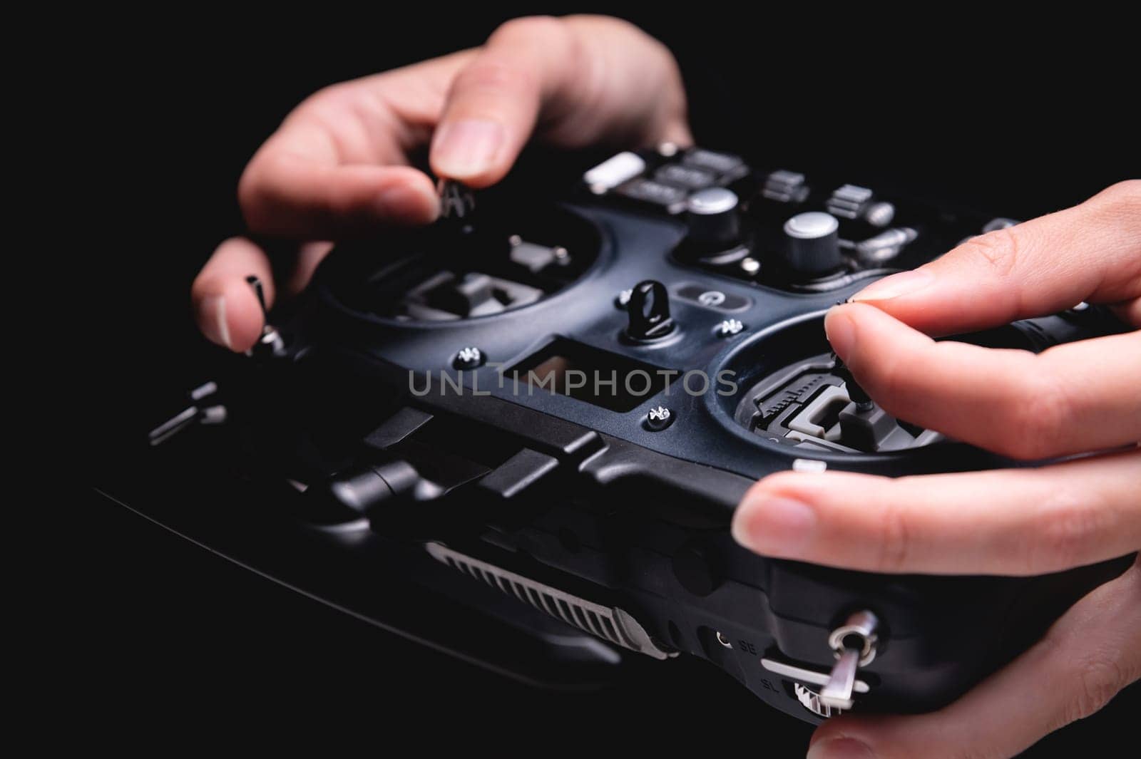 Close-up view of a woman operating the remote control of an FPV racing drone. Hands holding black fpv drone transmitter, on black background by yanik88