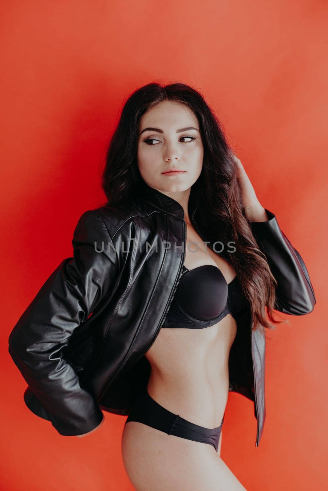 brunette girl in leather jacket and black lingerie on a red background by Simakov