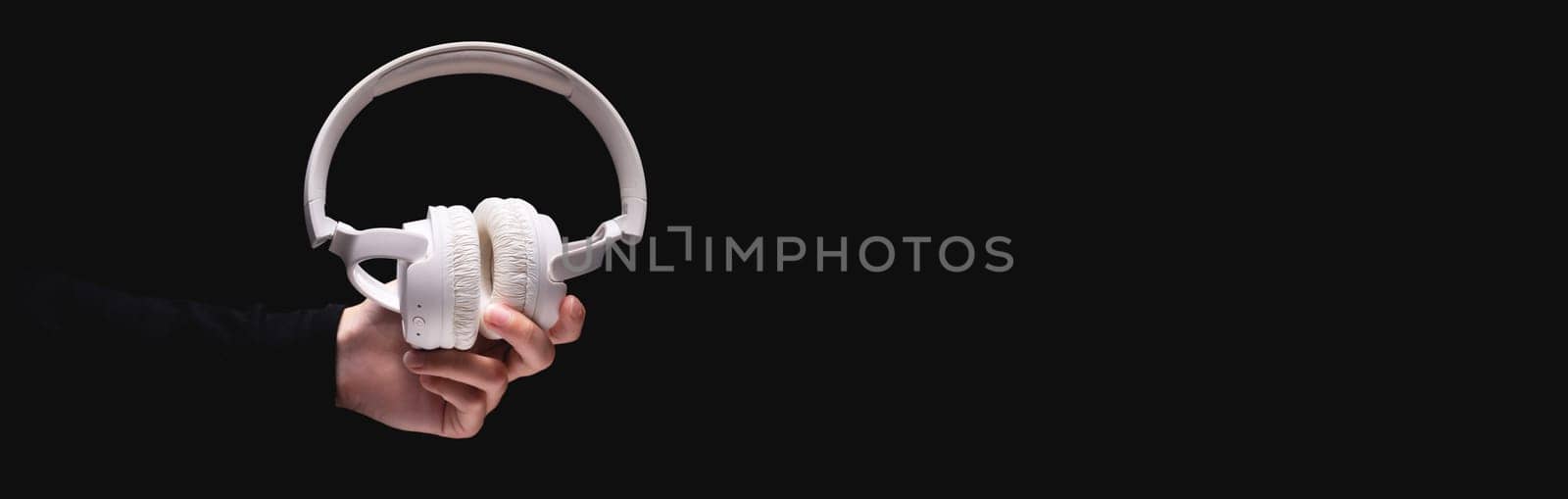 white headphones in a woman's outstretched hand on a dark background, banner for advertising.