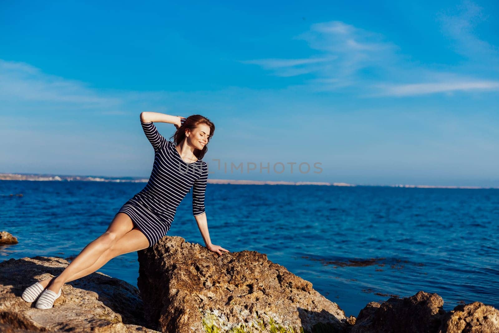 girl sits on the rocky beach enjoys sunshine 1