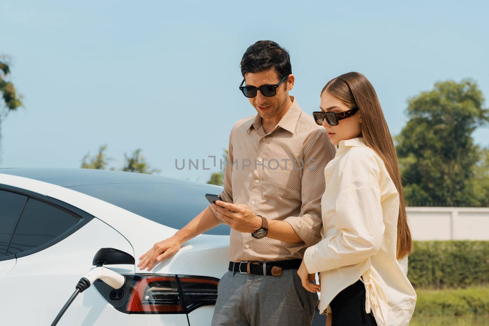 Young couple use smartphone to pay for electricity for EV car. Expedient by biancoblue