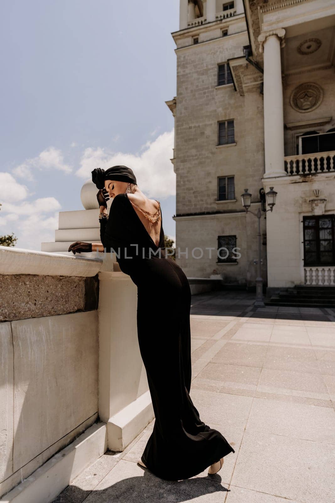 Stylish woman in the city. Fashion photo of a beautiful model in an elegant black dress posing against the backdrop of a building on a city street.