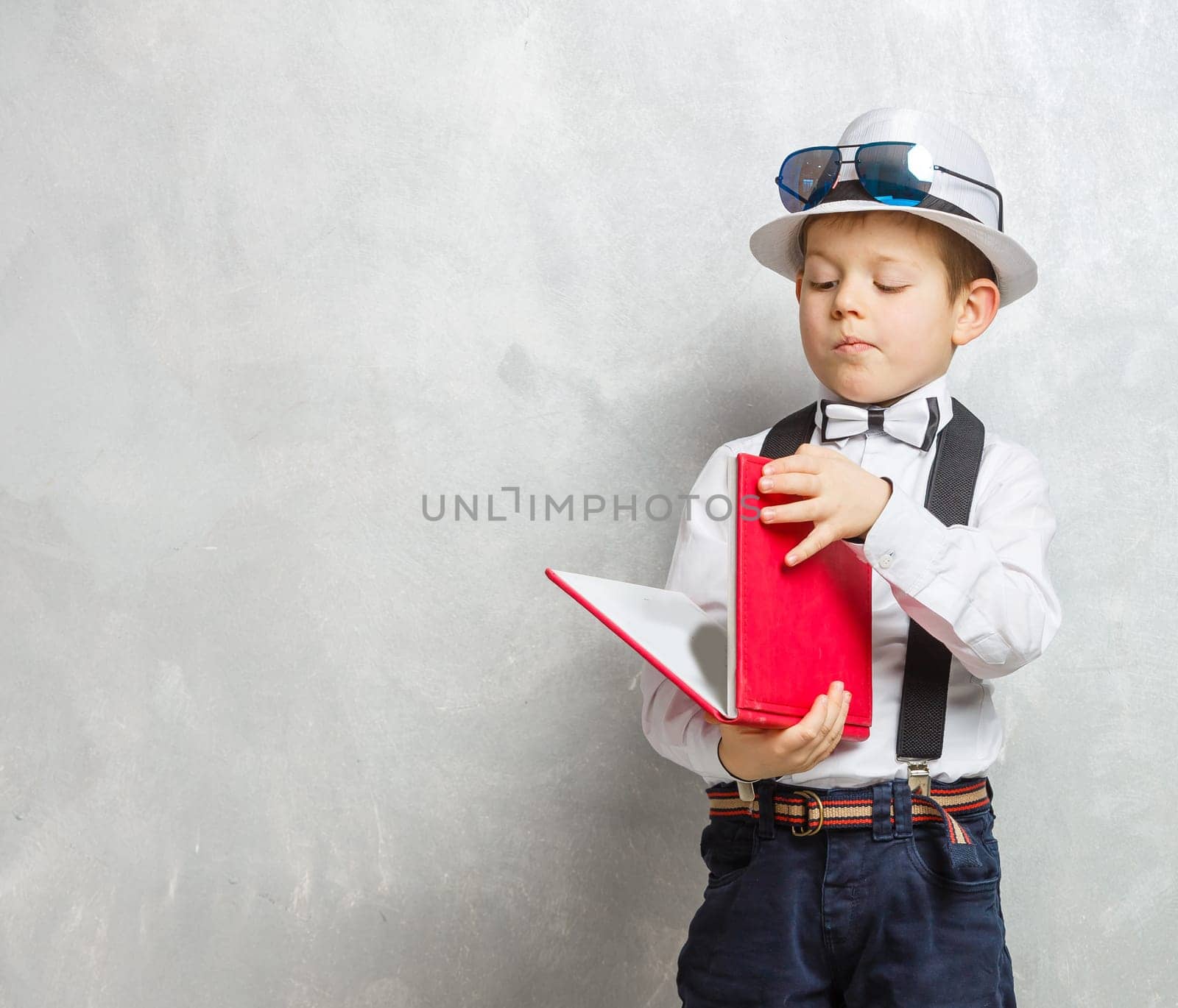 little schoolboy with a book on gray color background.