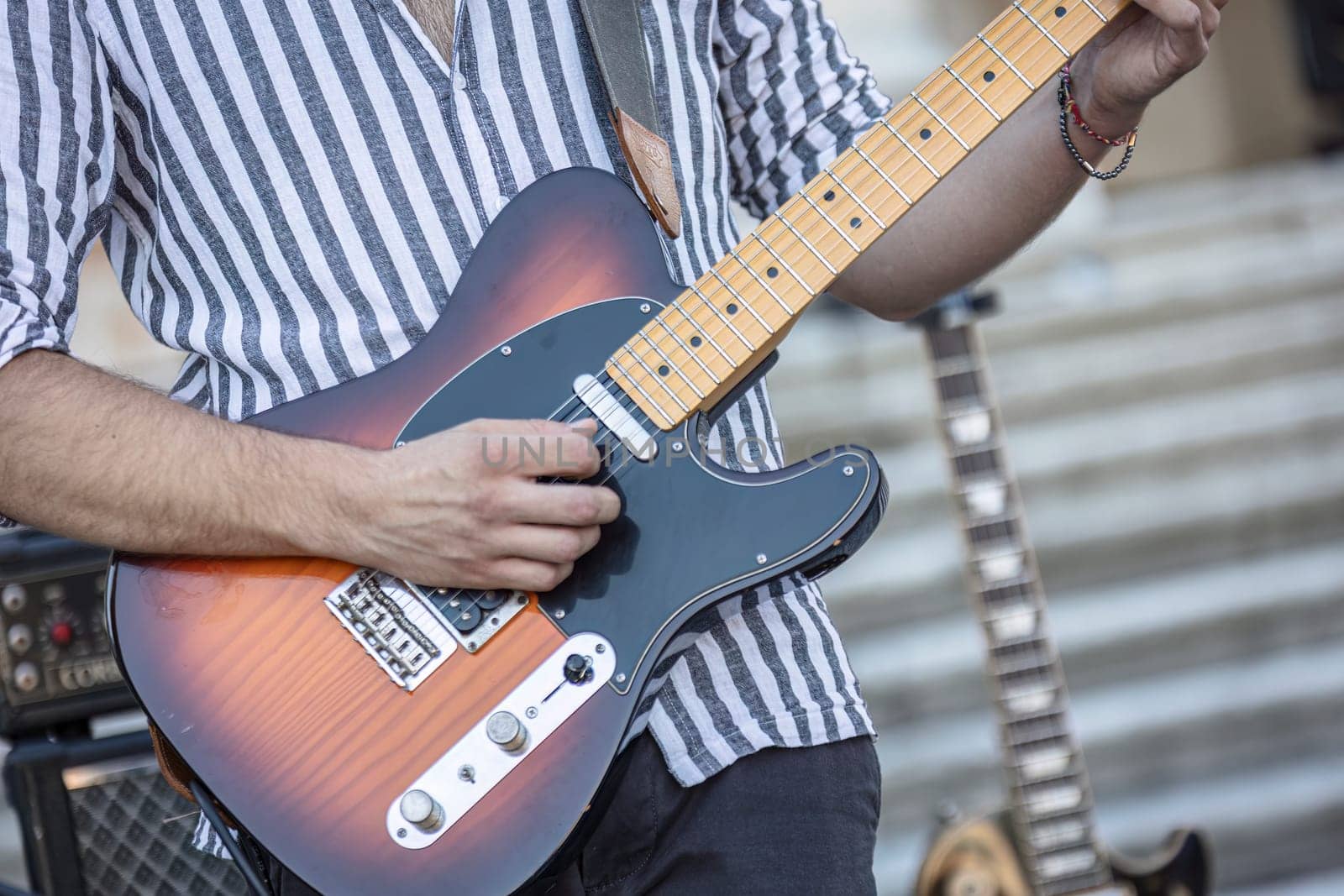 Close-up of a musician's hands playing the guitar during a live daylight performance.