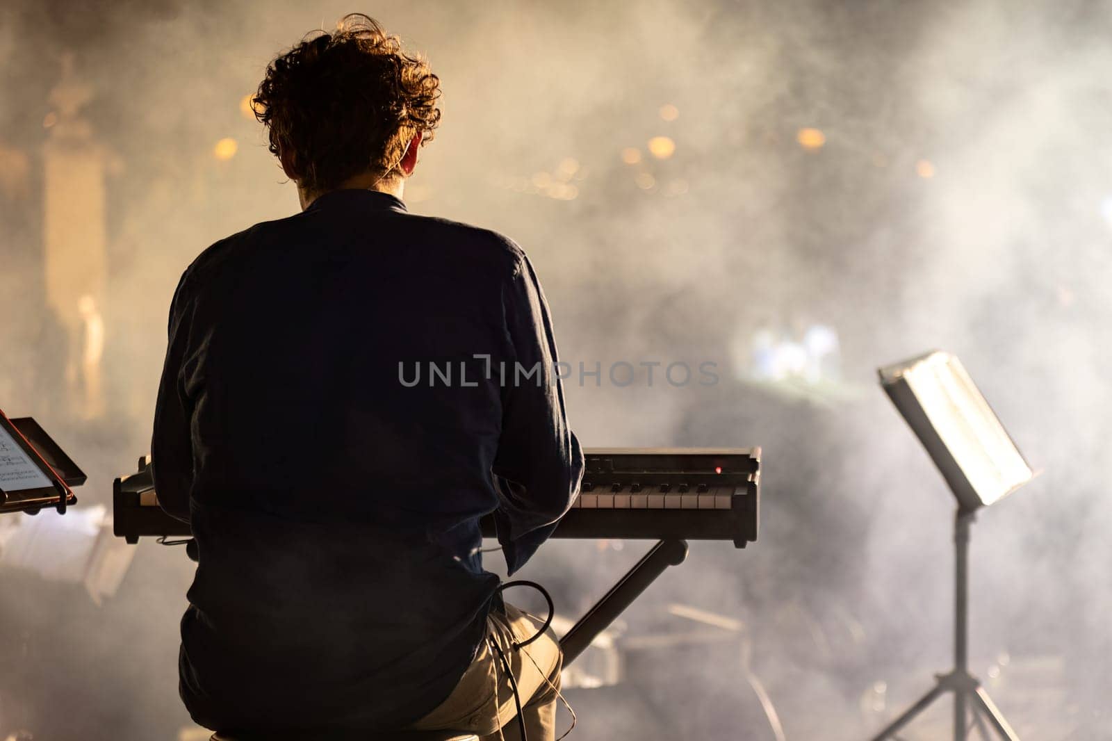 A pianist seen from behind, playing in a night concert with a mystical foggy atmosphere.