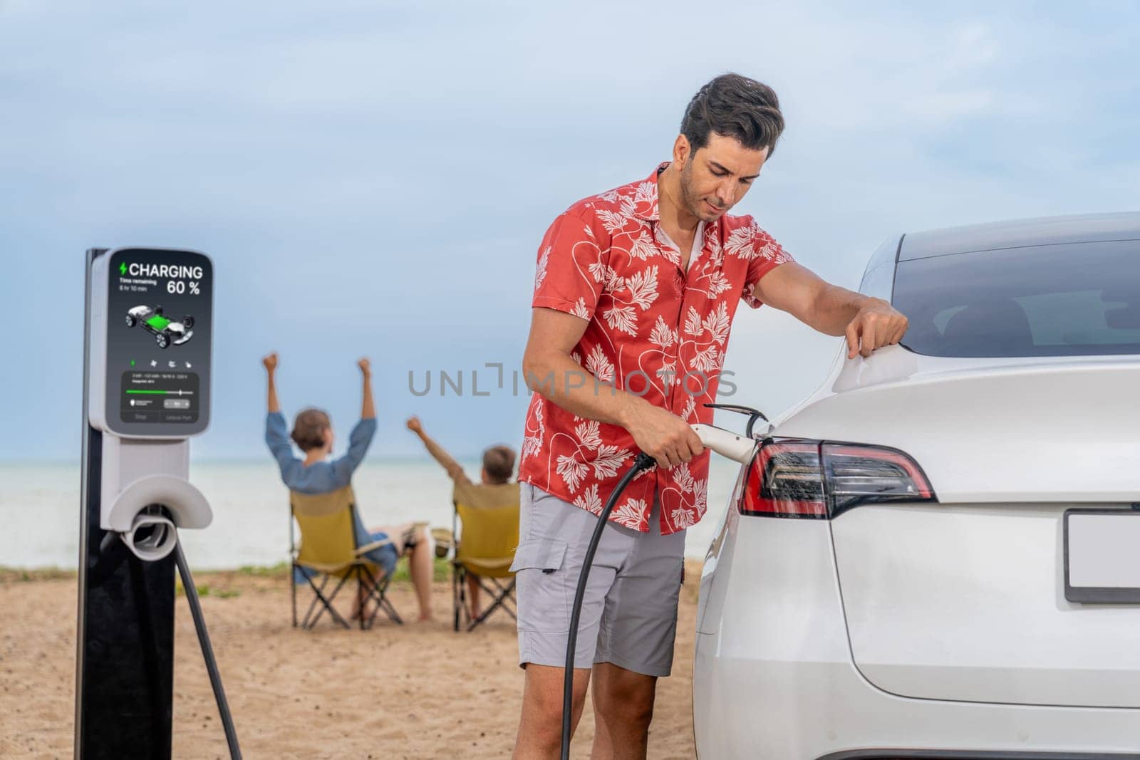 Family vacation trip traveling by the beach with electric car, dad or father recharge EV car while his family enjoy seascape beach. Family trip with alternative energy and eco-friendly car. Perpetual