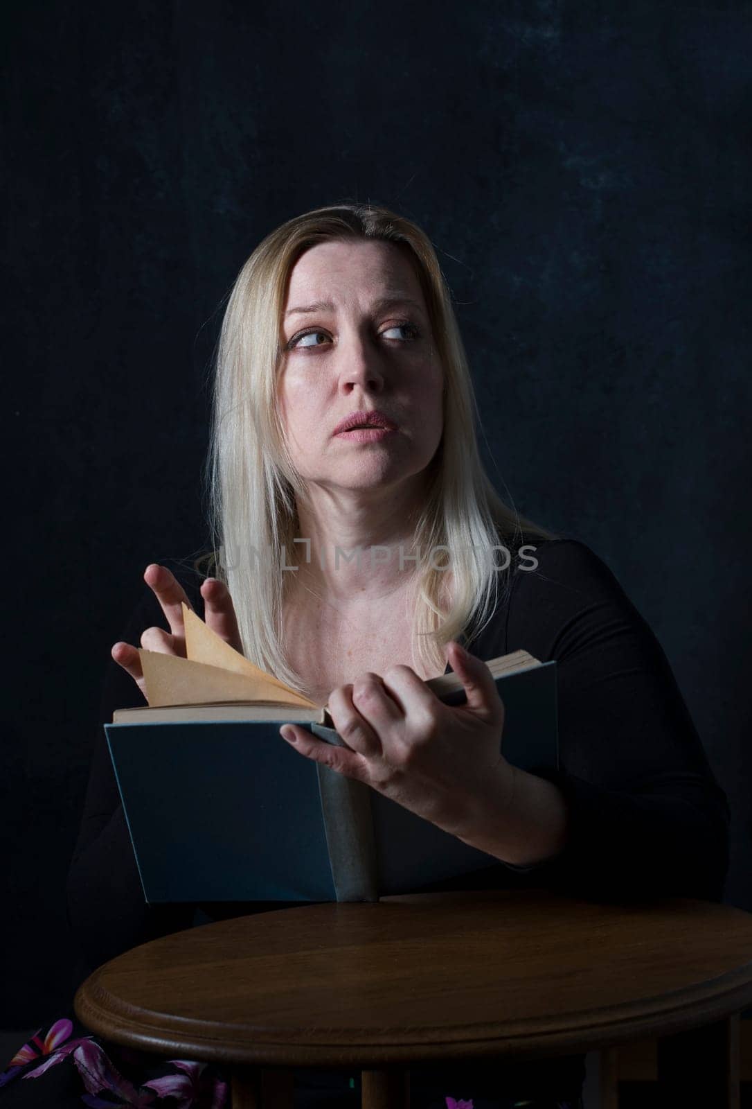 young blonde Caucasian woman reading a book in a dark room and listening to something alarming behind her, psychology by KaterinaDalemans