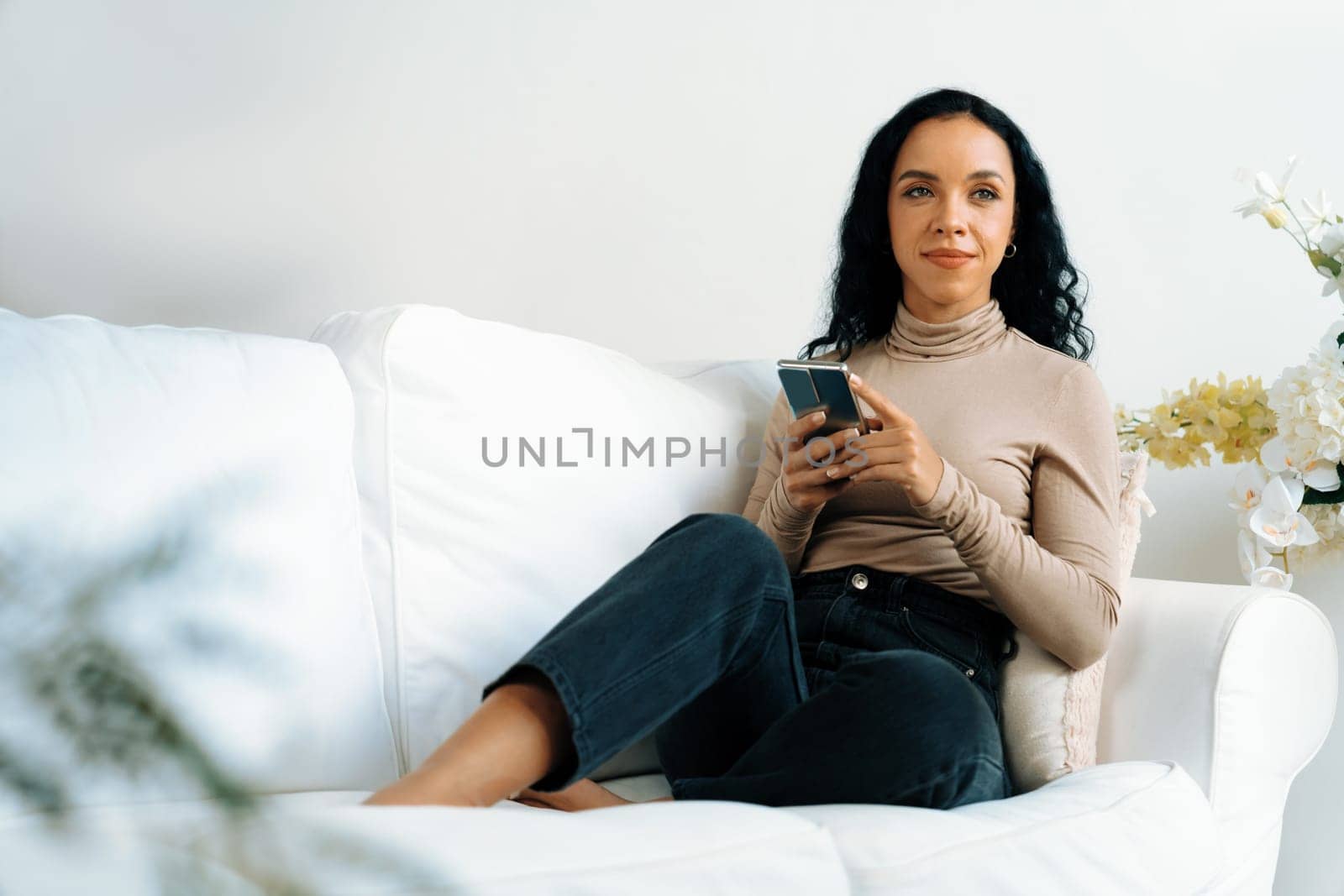 Relaxed young African American woman using crucial mobile phone on sofa couch by biancoblue