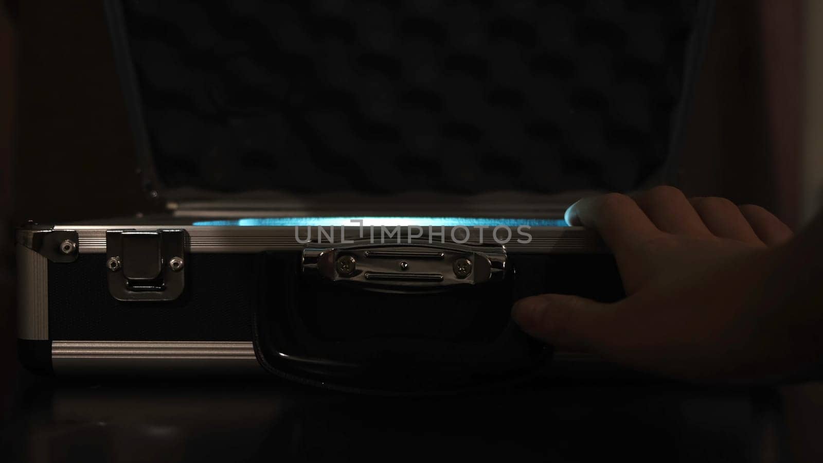 Close up of female hands opening silver metal suitcase with locking system. Opening aluminum carrying case to find shining mysterious object inside.