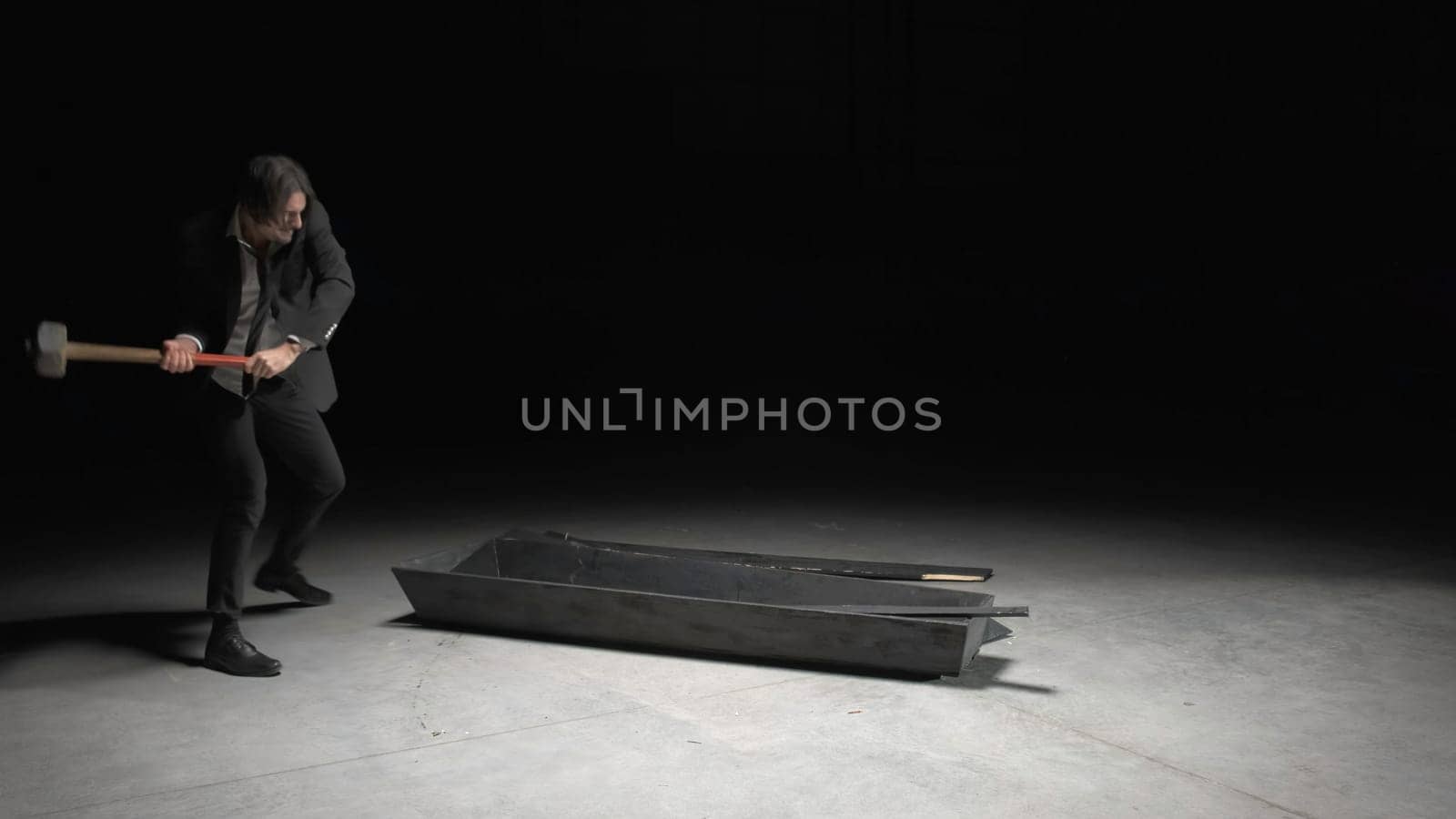 Man with sledgehammer. Stock footage. Man in dark room breaks wooden box out of anger. Man with hammer breaks wooden box.