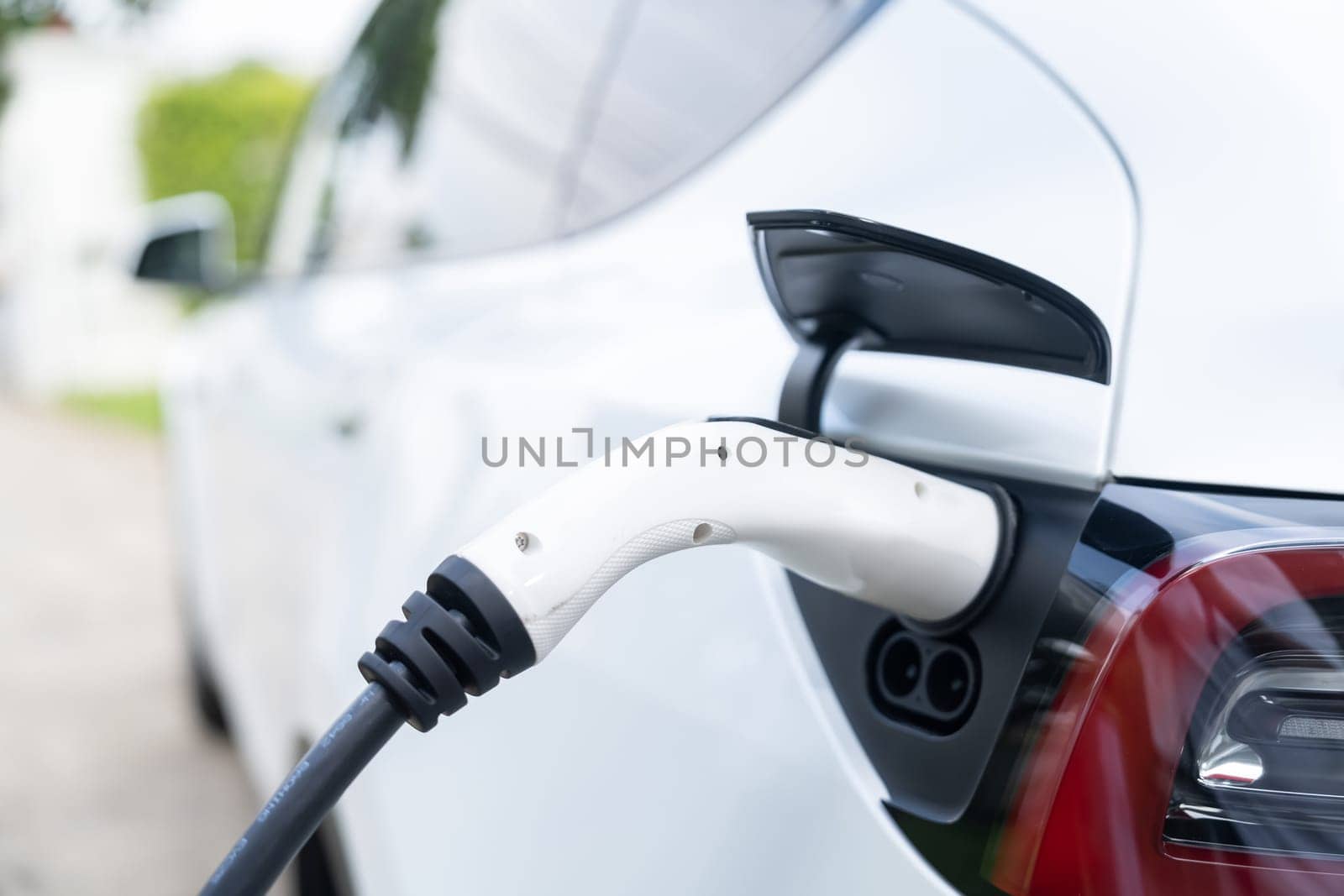 Closeup EV charger plug handle attached to electric vehicle port. Synchronos by biancoblue