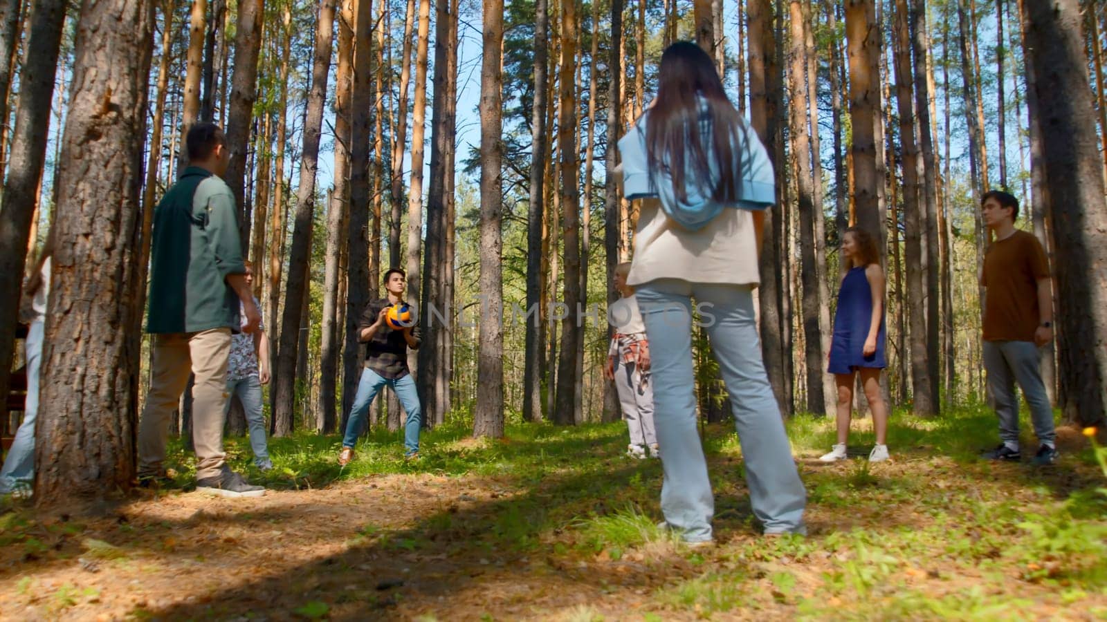 People have fun playing volleyball in park. Stock footage. Friends are actively playing volleyball in forest clearing. Fun ball games for group of friends in forest.