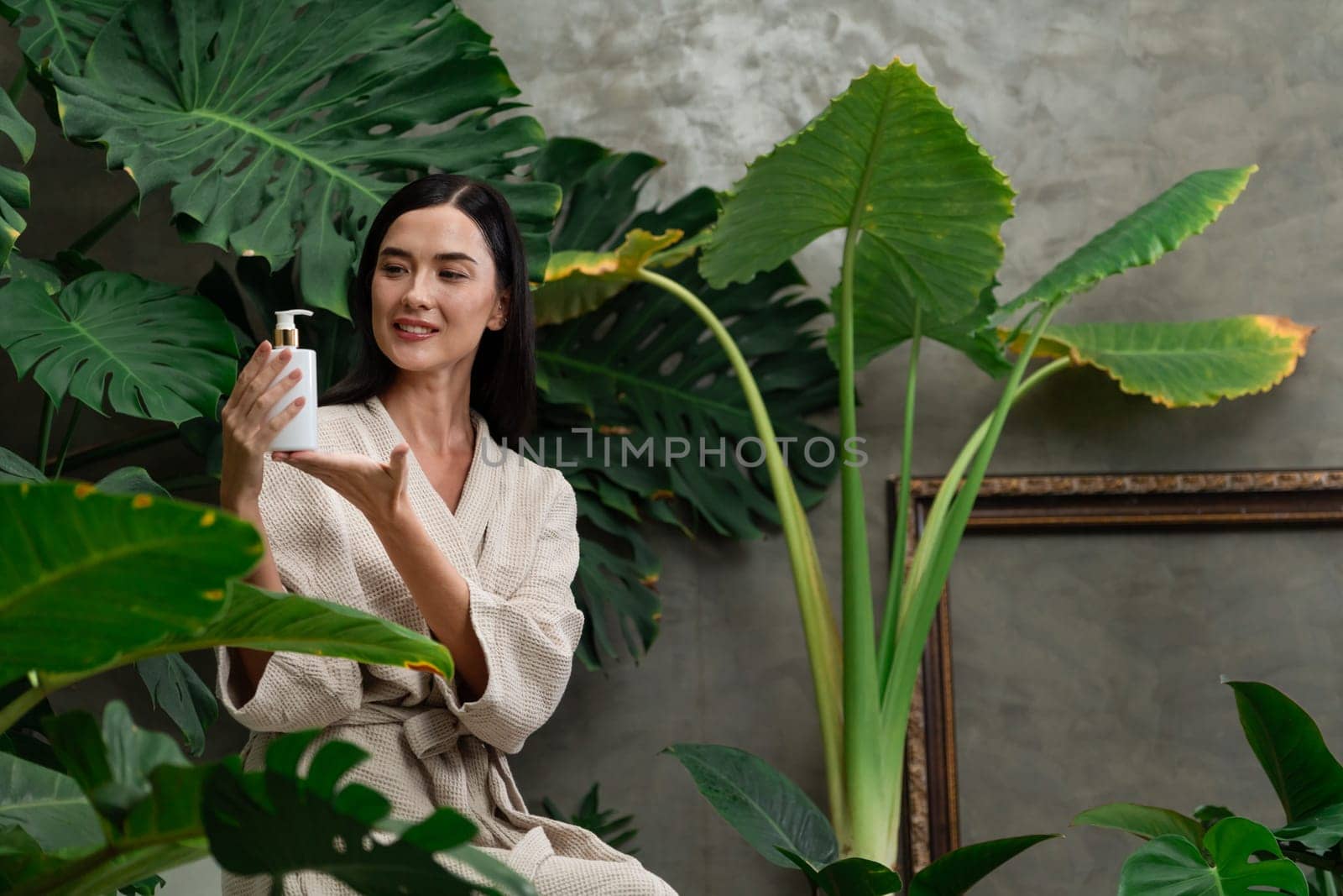 Tropical and exotic spa garden with bathtub in modern hotel or resort with woman in bathrobe holding beauty skincare product while enjoying leisure lush with greenery foliage background. Blithe