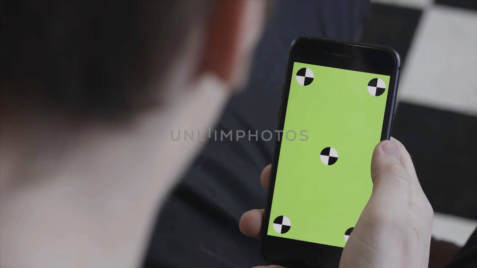Man hands using mobile smartphone with green screen, over the shoulder view. Stock footage. Close up of man scrolling and tapping on Iphone screen with chroma key. by Mediawhalestock
