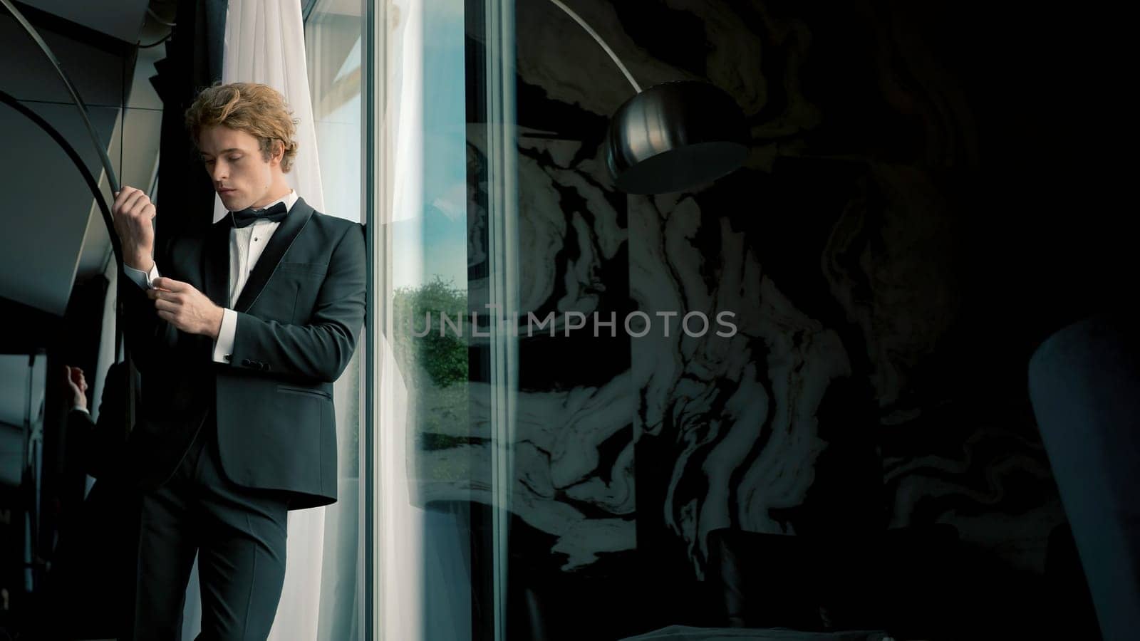 A man in a beautiful black suit with a watch.Action.A very cute man with long curly hair who poses for a photo shoot in different poses. High quality 4k footage