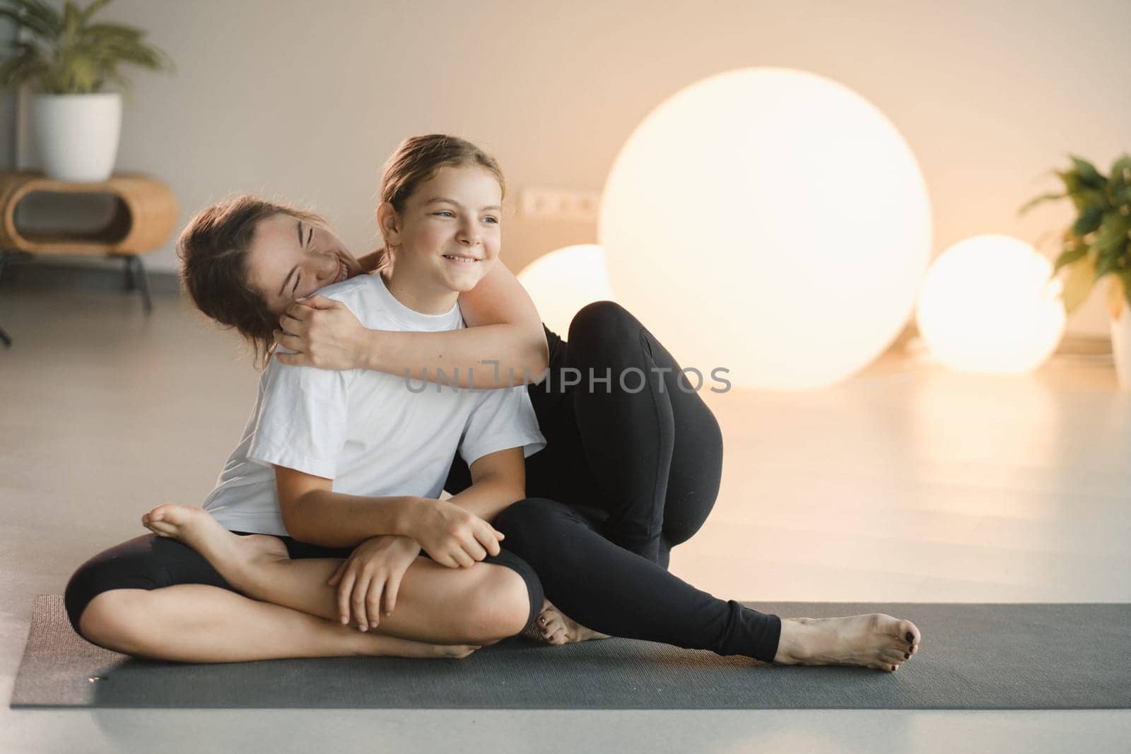 portrait of a mother and daughter of a teenager in sports clothes hugging, who are together in a fitness room. the concept of family sports by Lobachad