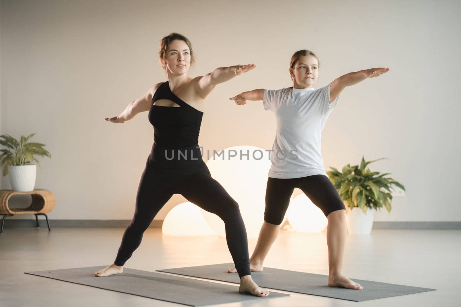 Mom and teenage daughter do gymnastics together in the fitness room. A woman and a girl train in the gym by Lobachad