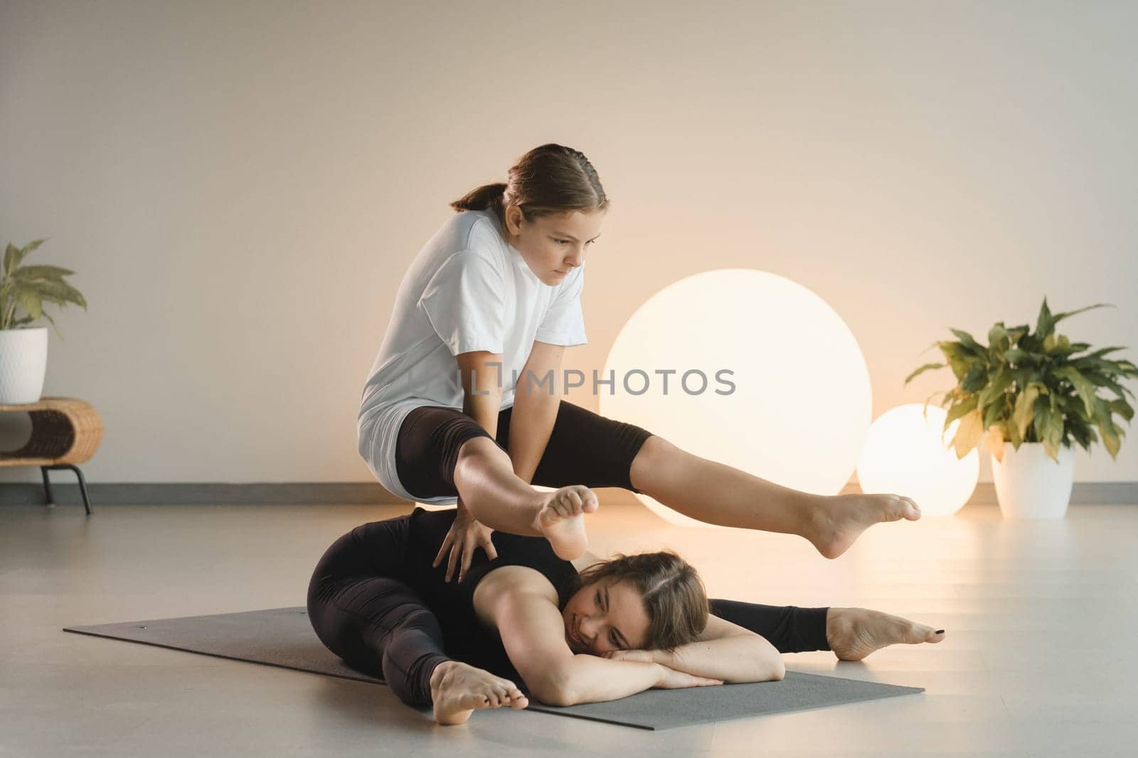 Mom and teenage daughter do gymnastics together in the fitness room. A woman and a girl train in the gym by Lobachad