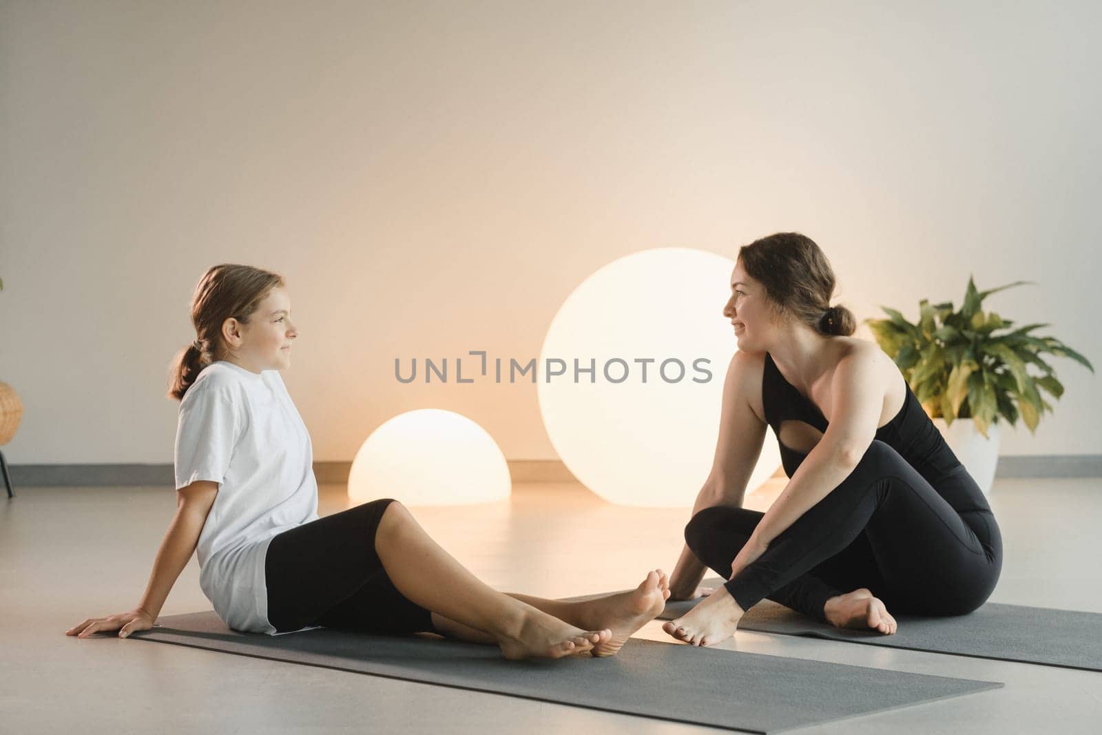 Mom and teenage daughter do gymnastics together in the fitness room. A woman and a girl train in the gym by Lobachad