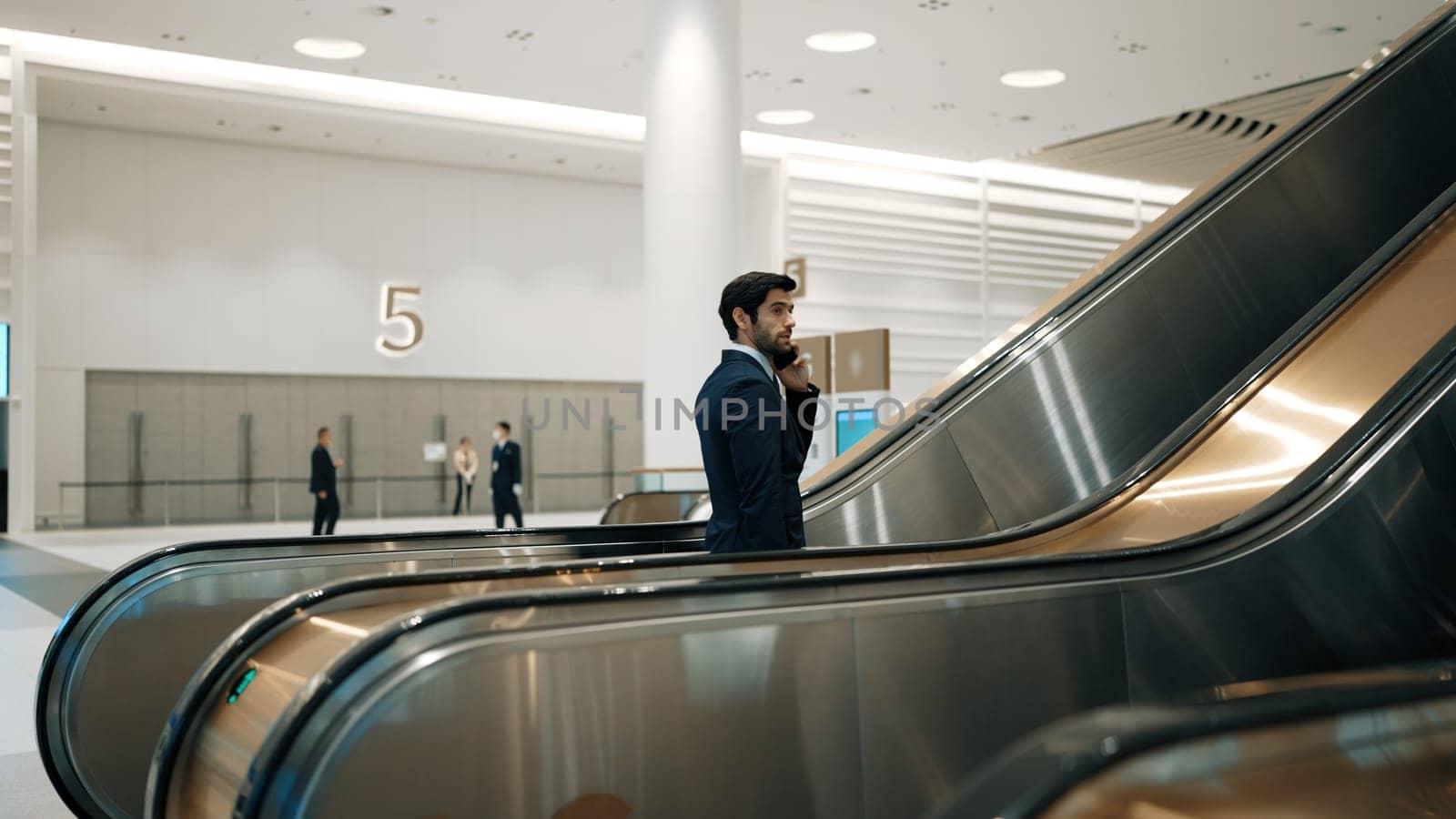 Skilled leader walking at escalator while calling his business team. Exultant. by biancoblue