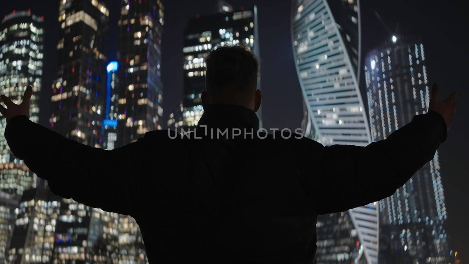 Guy raising hands on background of city. Action. Man solemnly raises hands on background of night city. Man raised hands on background of modern high-rises at night.