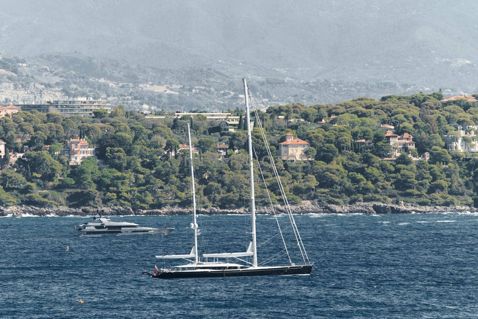 Monaco, mega yacht and huge sail boat are in sea at sunny day, island is nearby, huge motor boat, wealth life of billionaires, mountains on background. High quality photo