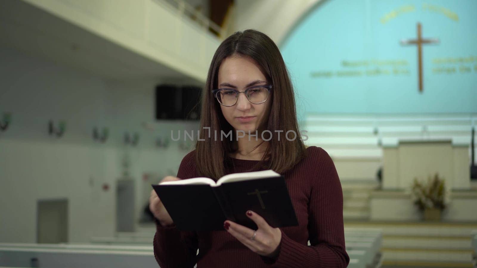 A young woman reads the Bible against the background of a cross in a church. A Protestant girl with glasses reads the Bible in church. 4k