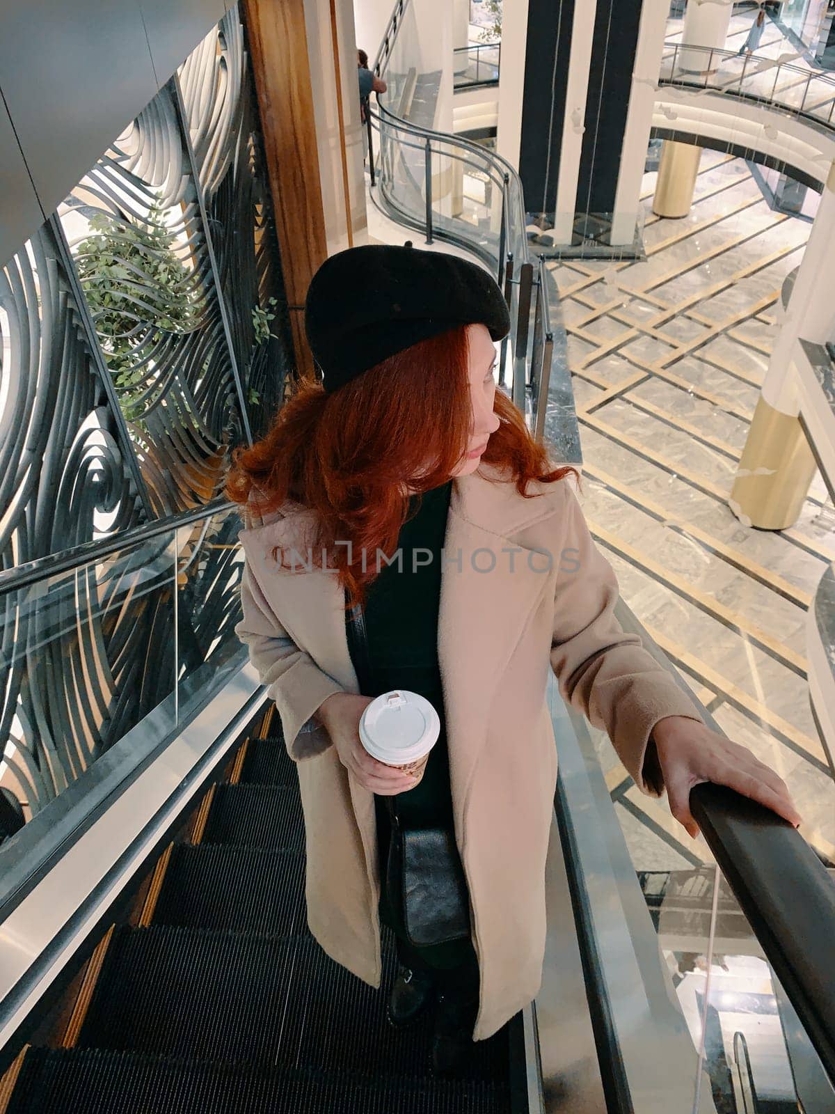 Shopping time. Red-haired woman on the escalator.
