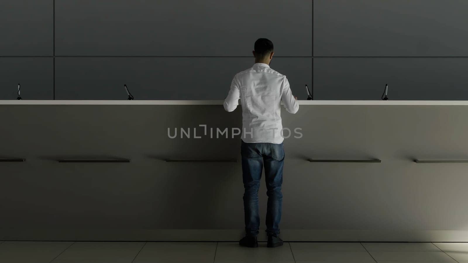Minimalistic interior of a hotel lobby with the reception desk. HDR. Rear view of a businessman in white shirt going to the receptionist and asking something
