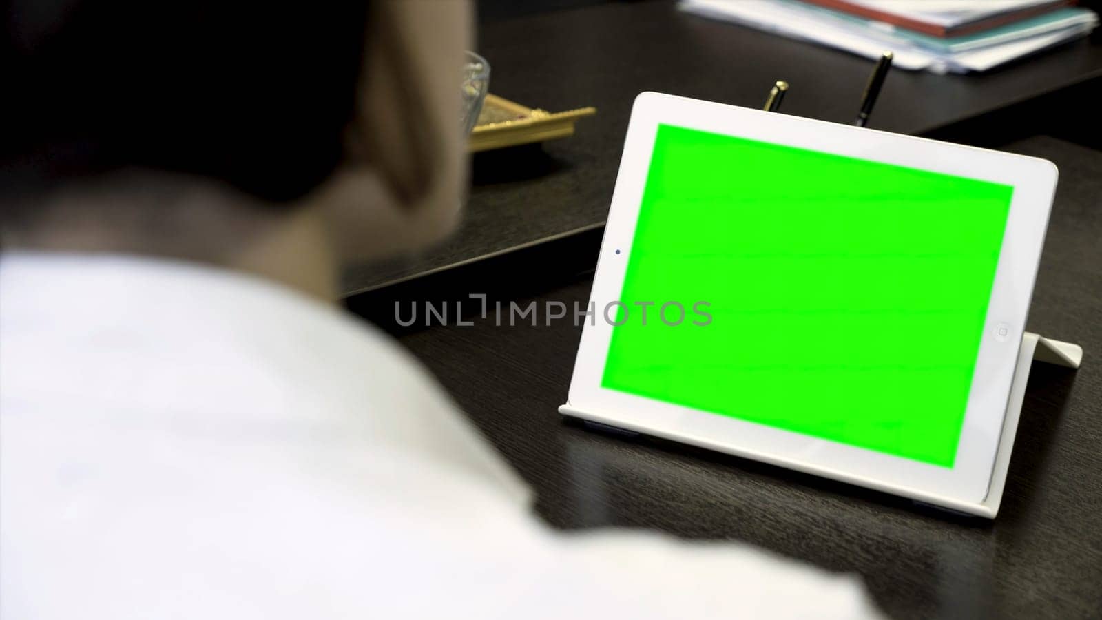 Close up for a woman looking at a white tablet with a green screen. Girl in white shirt working in office in front of tablet with chroma key, rear view