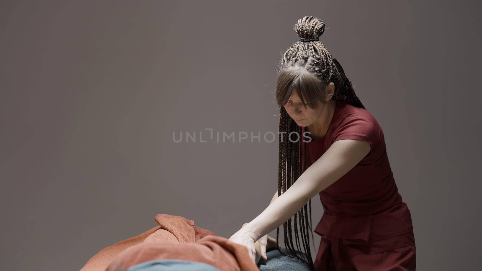 Wellness massage procedure. Action.A woman with long pigtails in a red suit is doing a massage on the couch. High quality 4k footage