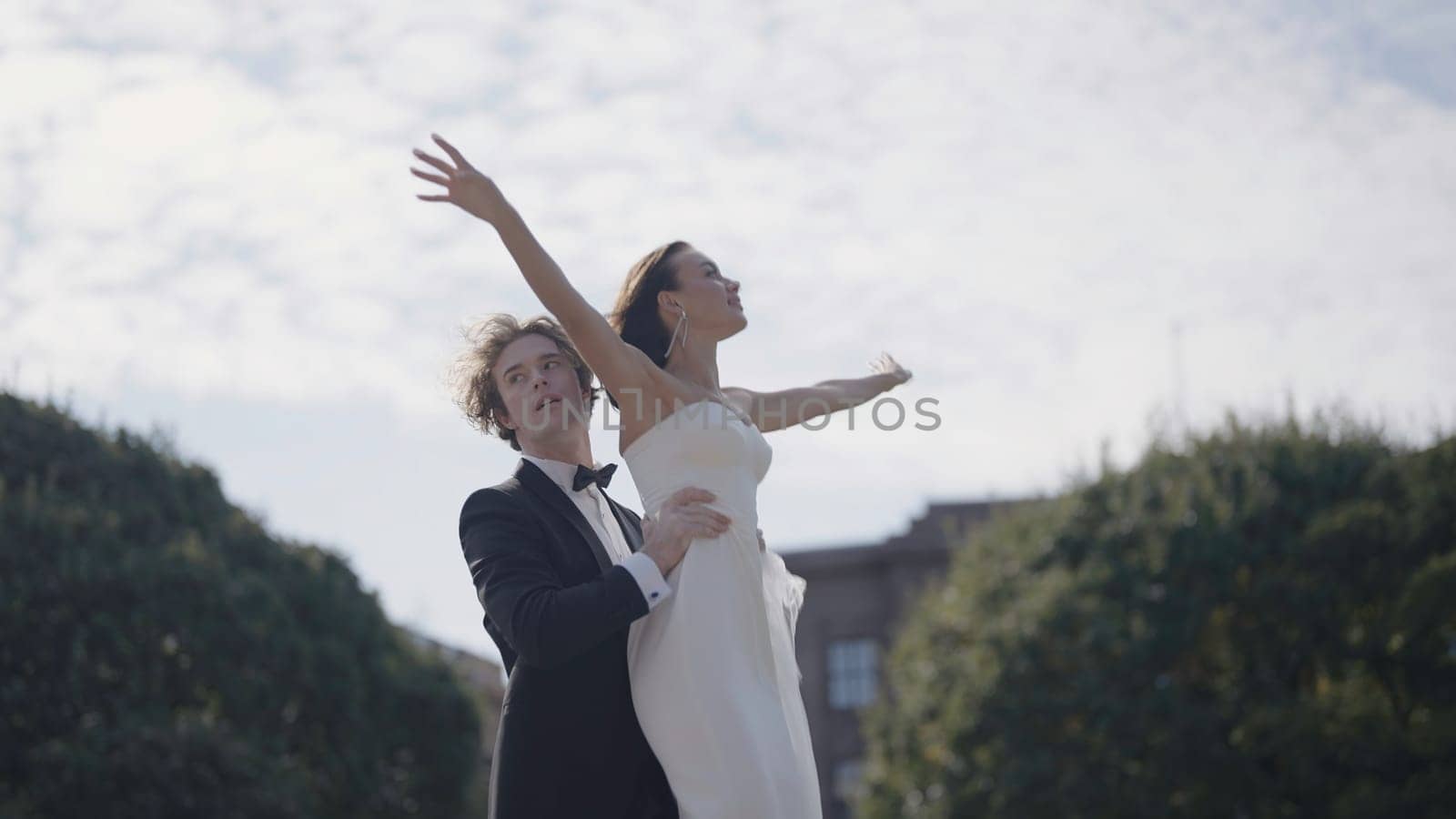 Photo shoot of newlyweds on street. Action. Groom lifts bride for beautiful photo. Groom raised bride like bird on background of park on sunny day.