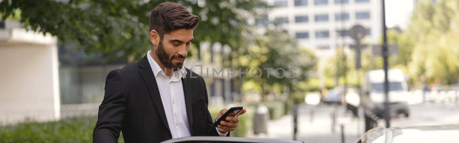 Focused male manager standing near car with phone before sit inside. High quality photo