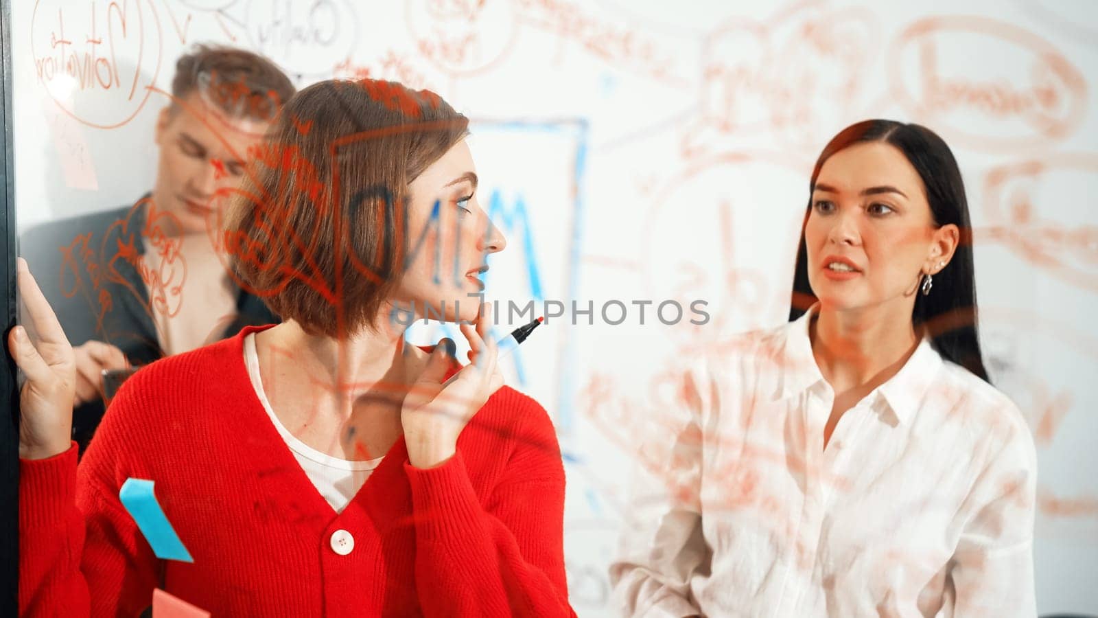 Professional business team brainstorming and working together about marketing project. Female caucasian leader writing idea on stick note while coworker present her idea confidently. Immaculate.