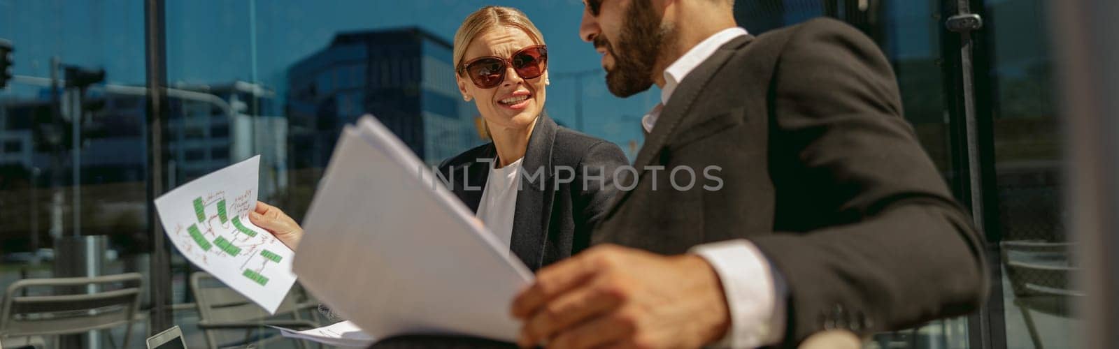 Business colleagues working with documents sitting outside of office on cafe terrace