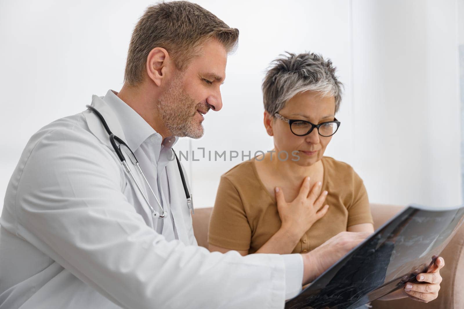 Male doctor explaining x-ray result for sick female patient in hospital office. High quality photo