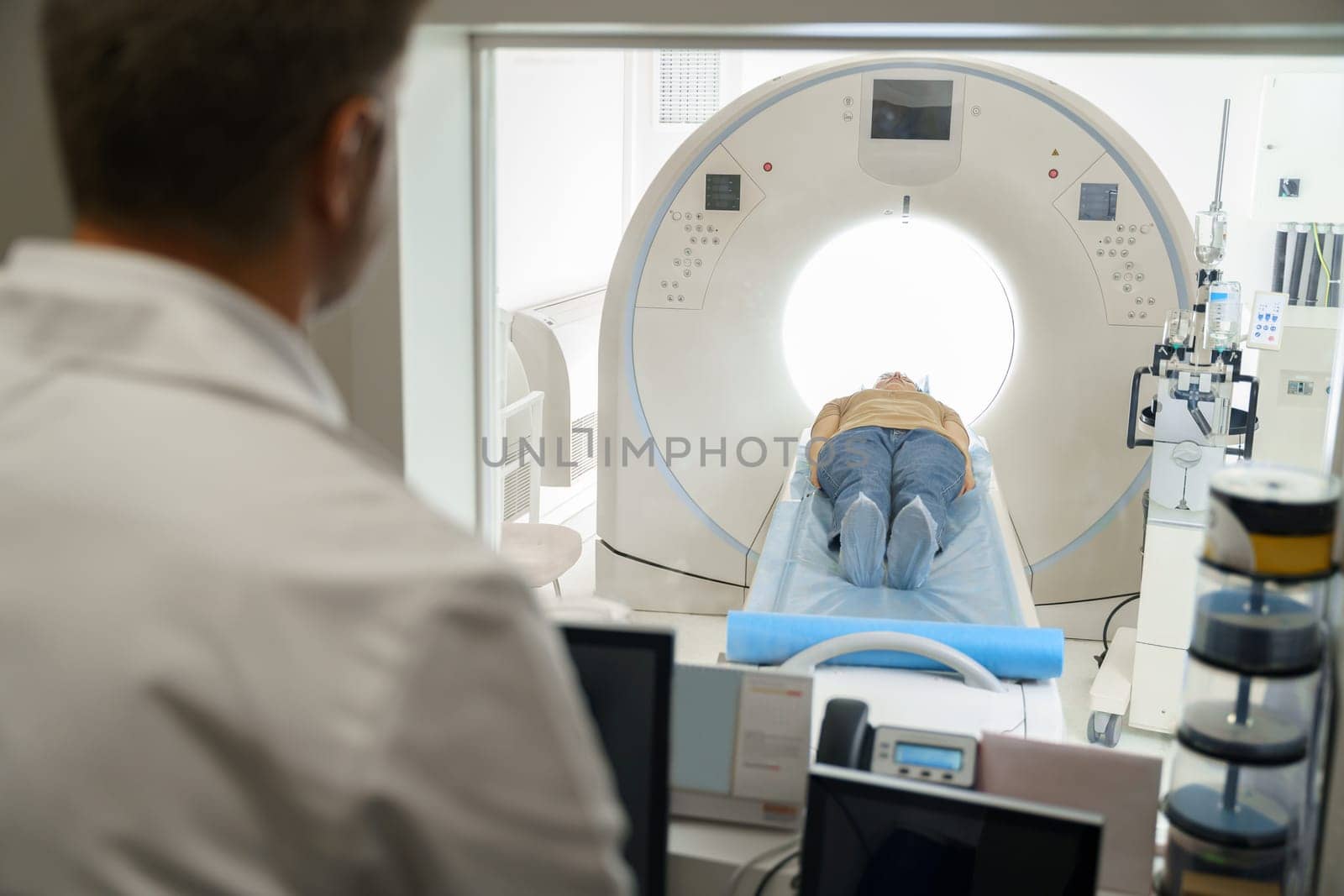 Radiologist controls MRI or CT Scan with patient undergoing procedure. High Tech medical equipment
