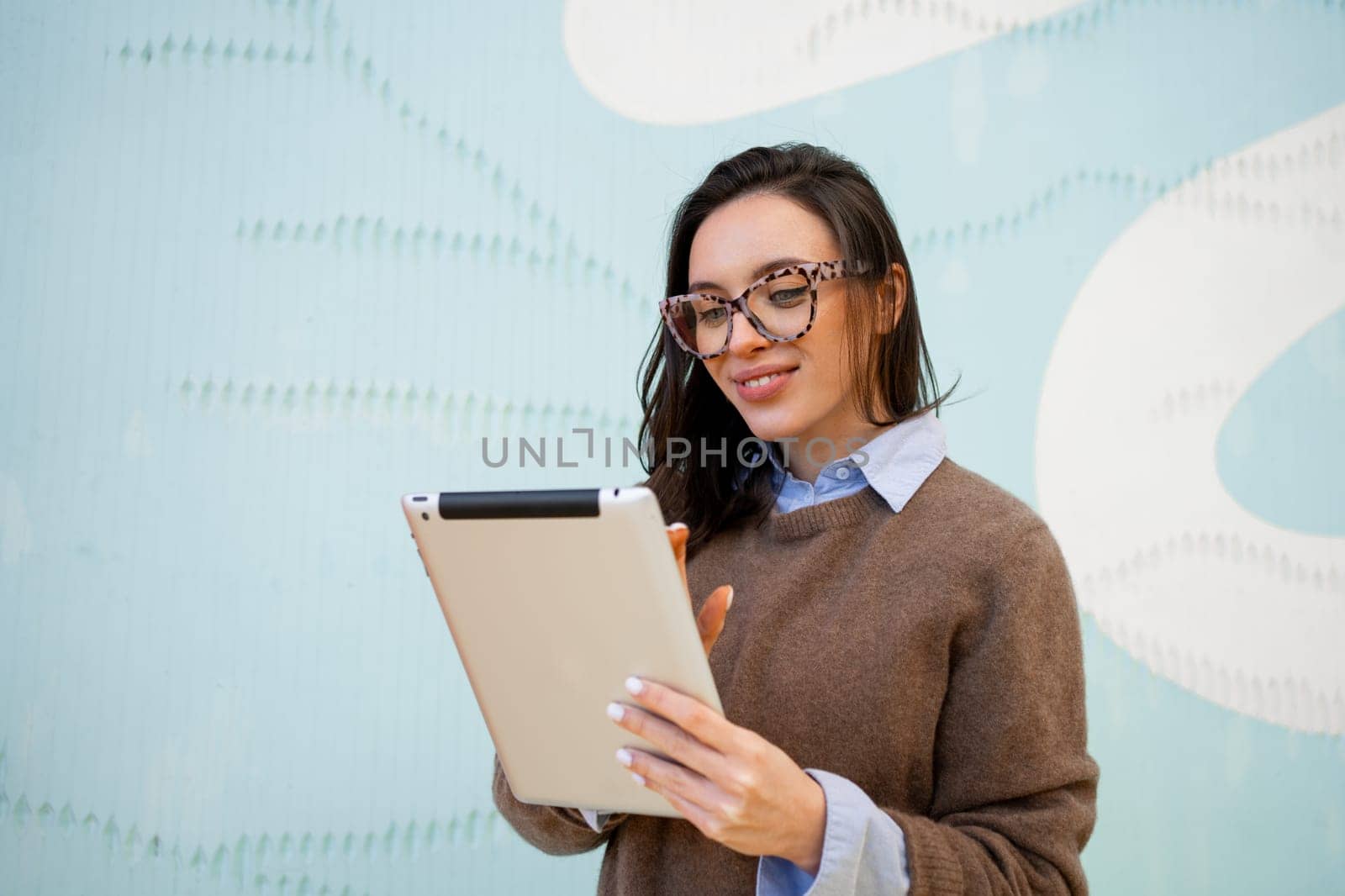Formally dressed woman smiling glasses and marks tasks on tablet. Woman at work looking in tablet is dressed in formal wear and glasses. Young adult woman smiles and remotely sends report